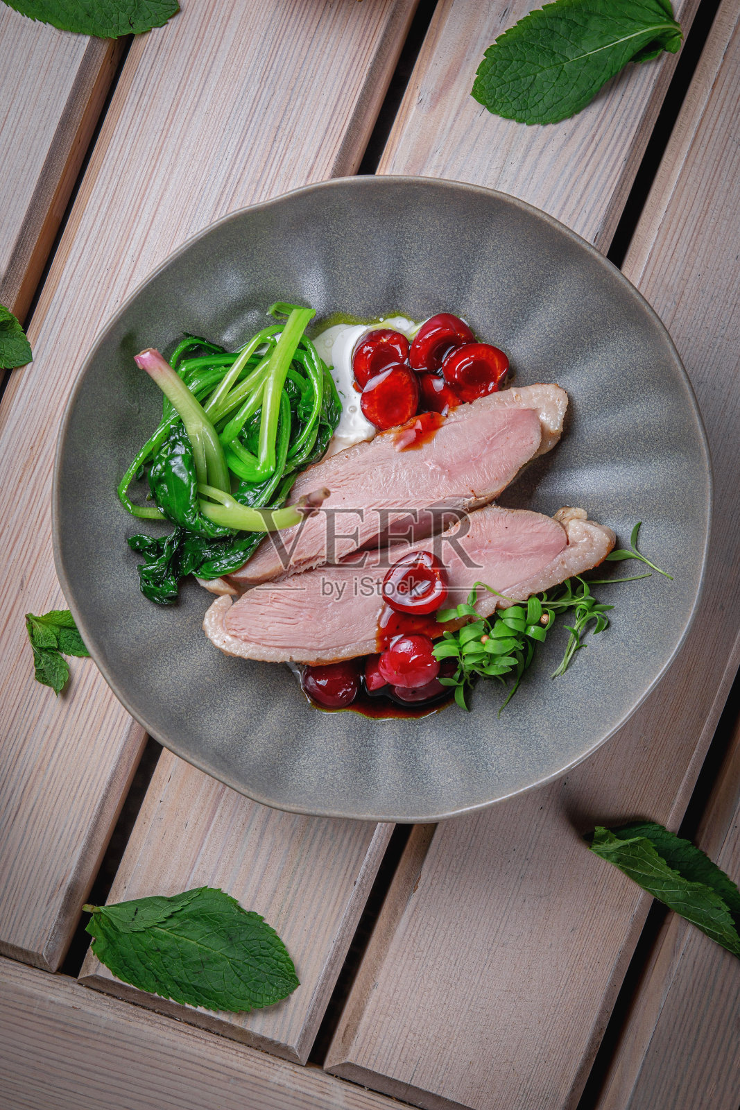 嫩鸭肉和腌樱桃配香草,放在木桌上的棕色陶盘里照片摄影图片