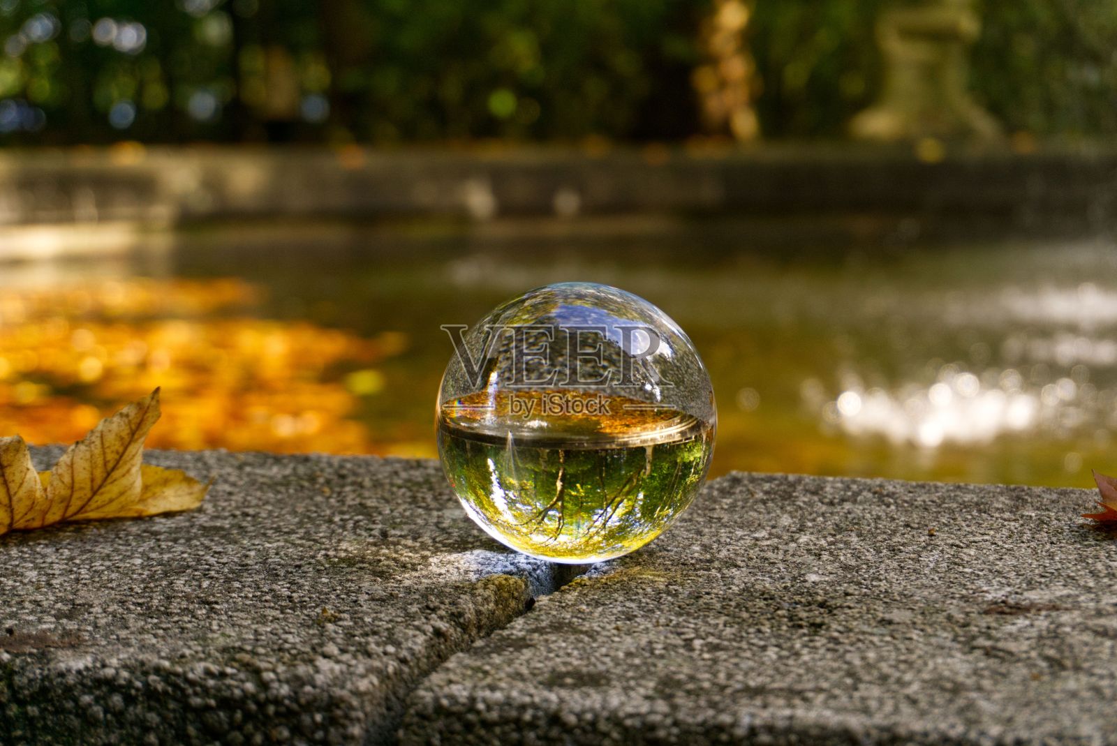 一个清晰的反射玻璃球在石头表面反射公园喷泉的特写镜头照片摄影图片