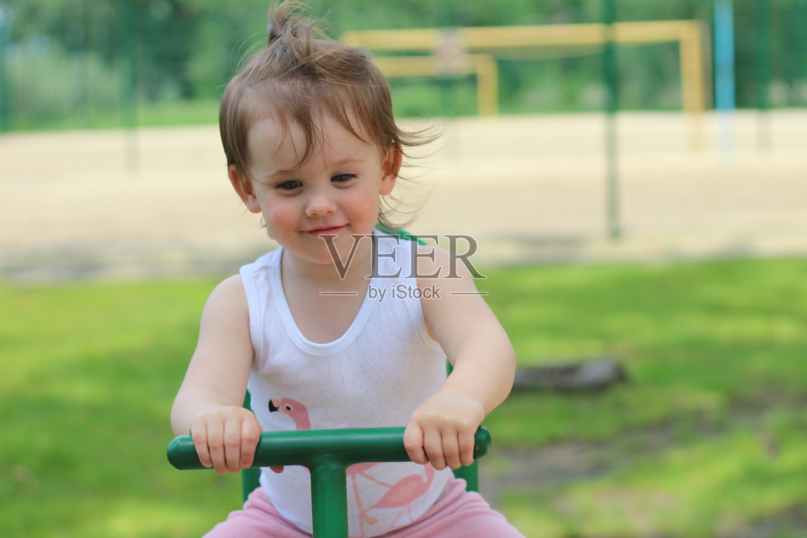 可爱开朗的幼儿园小女孩穿着t恤在公园里荡秋千,背景是操场照片摄影图片