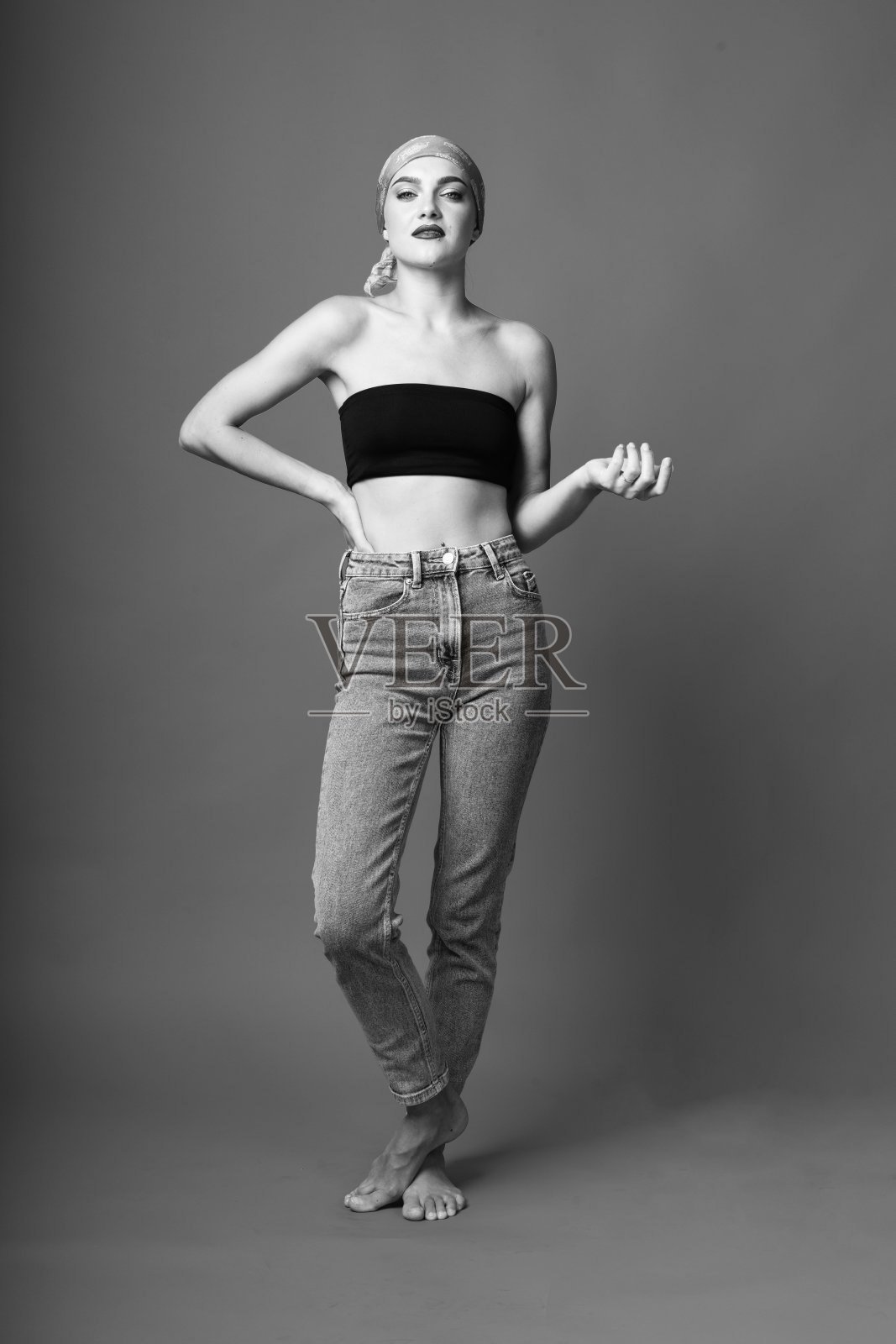 肖像美丽的女人与紧黑色胸罩和牛仔裤站在灰色的工作室背景照片摄影图片