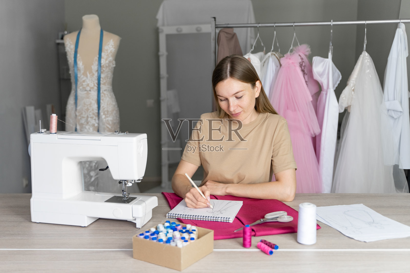 缝纫车间里的年轻女工正在为一件新衣服画草图。照片摄影图片