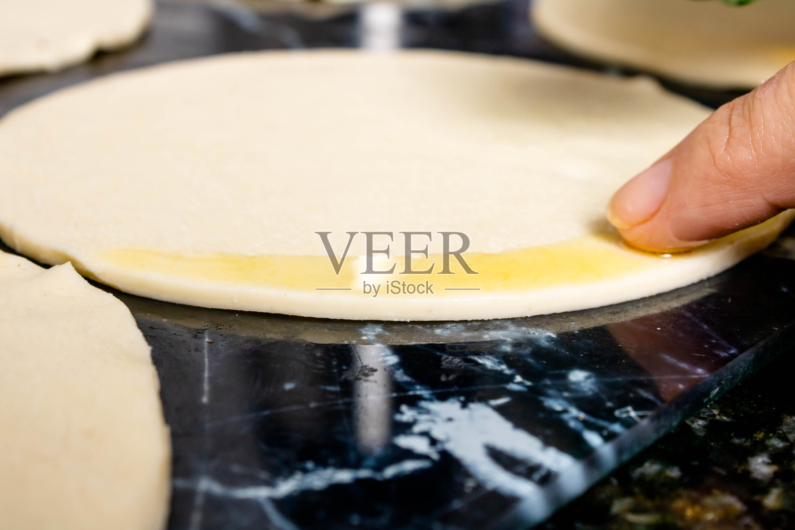 酥皮准备,用白女人的手指在酥皮边缘抹上橄榄油。提到家里厨房里的食物准备,快速实用的食物。照片摄影图片