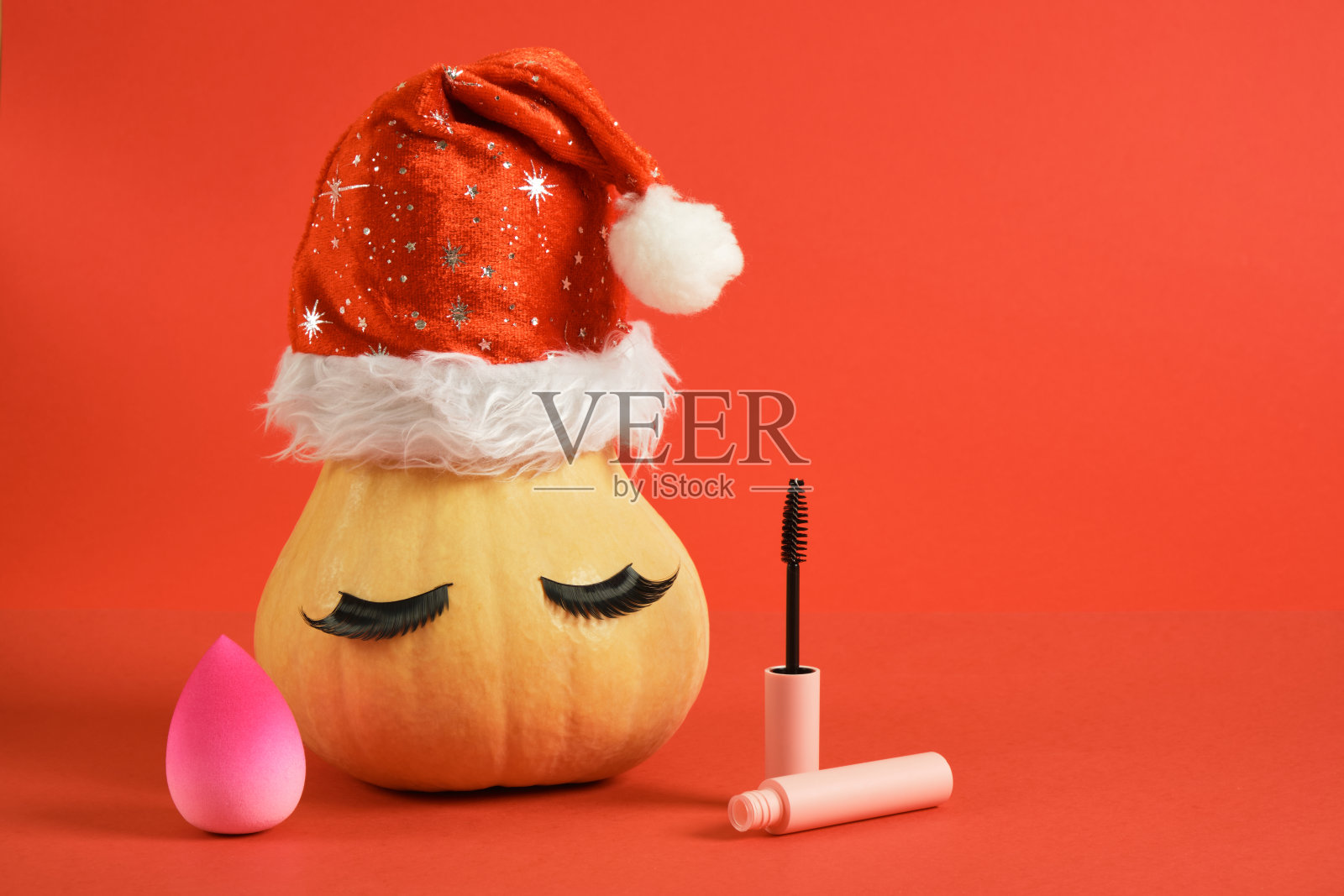 粉色化妆海绵,粉色化妆包装的睫毛膏,戴圣诞帽的南瓜和假睫毛照片摄影图片