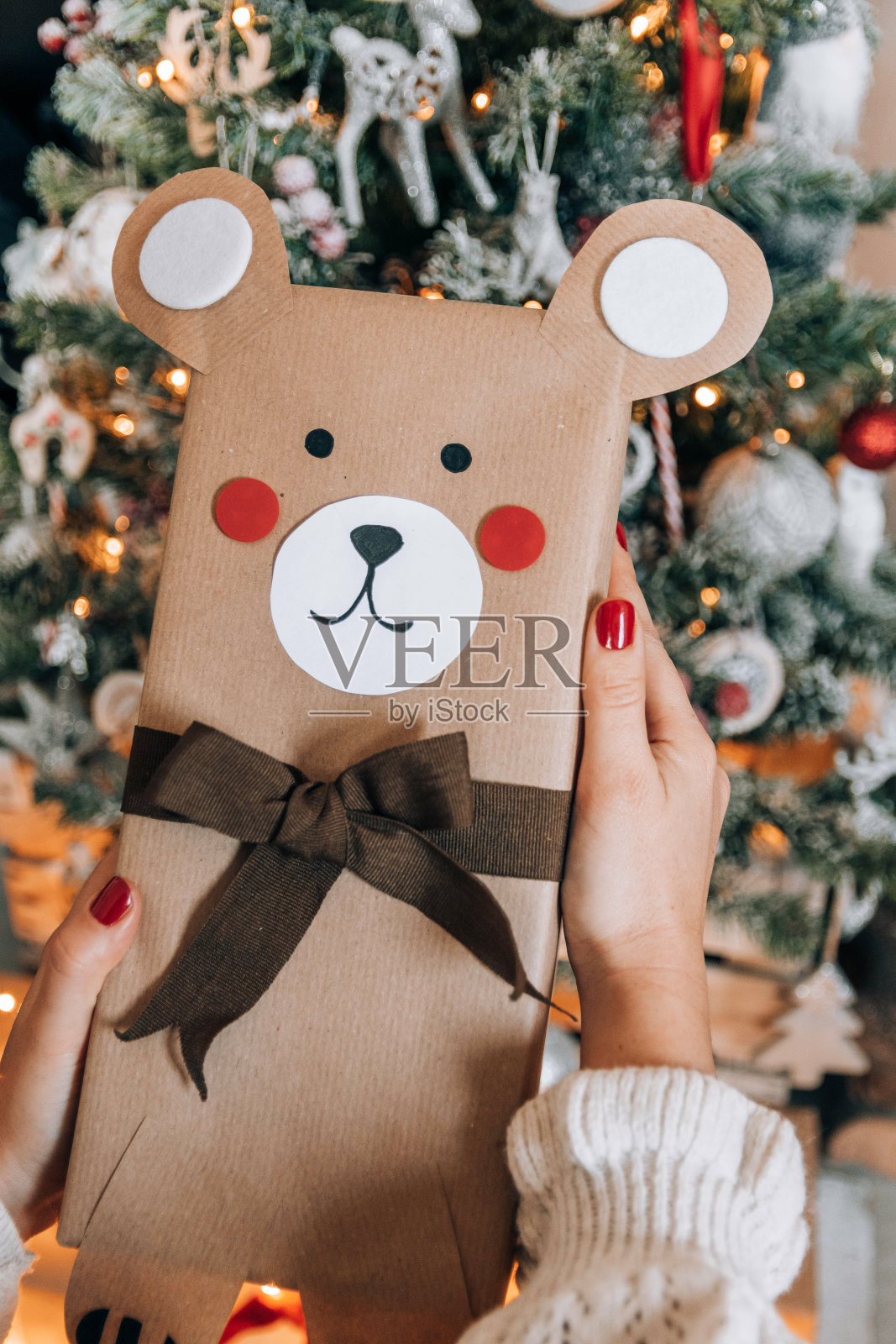 一个人拿着包装精美的礼物,礼物被装饰成用黑丝带装饰的熊,靠近圣诞树照片摄影图片