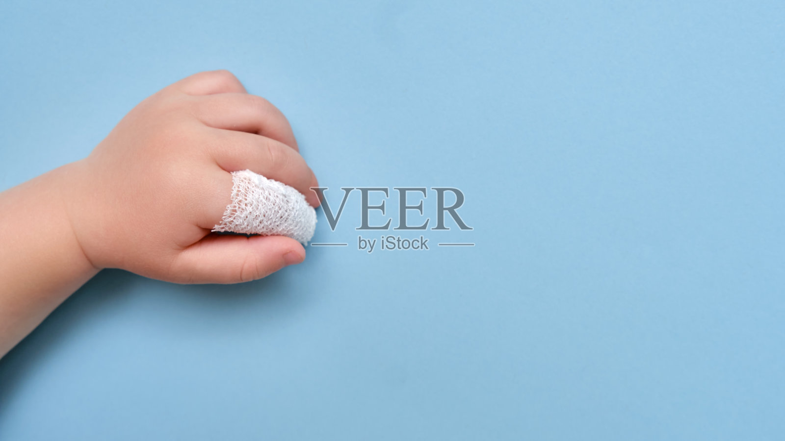 婴儿的手与绷带的手指在工作室蓝色的背景,复制空间。儿童食指受伤,用白色绷带包扎照片摄影图片