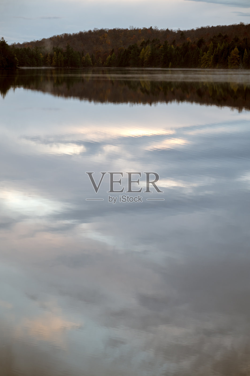 平静的湖面上,绿树成荫的海岸线倒映着彩云。照片摄影图片