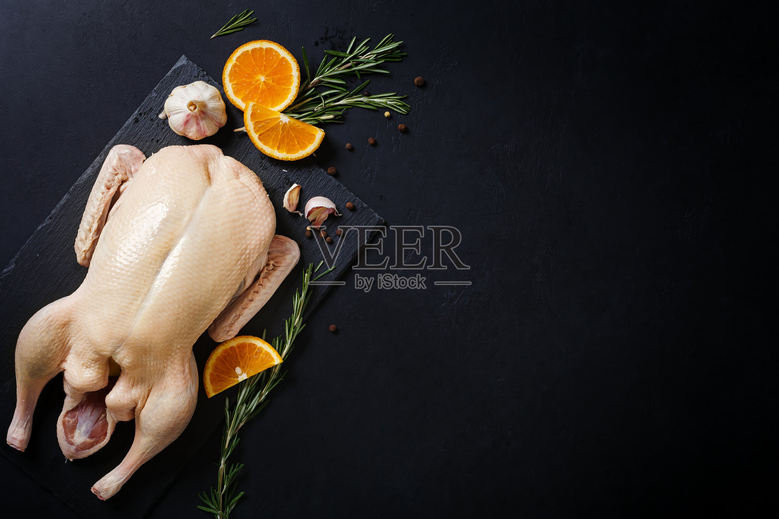 生的和未煮的整只鸭子放在石板上,黑色背景照片摄影图片