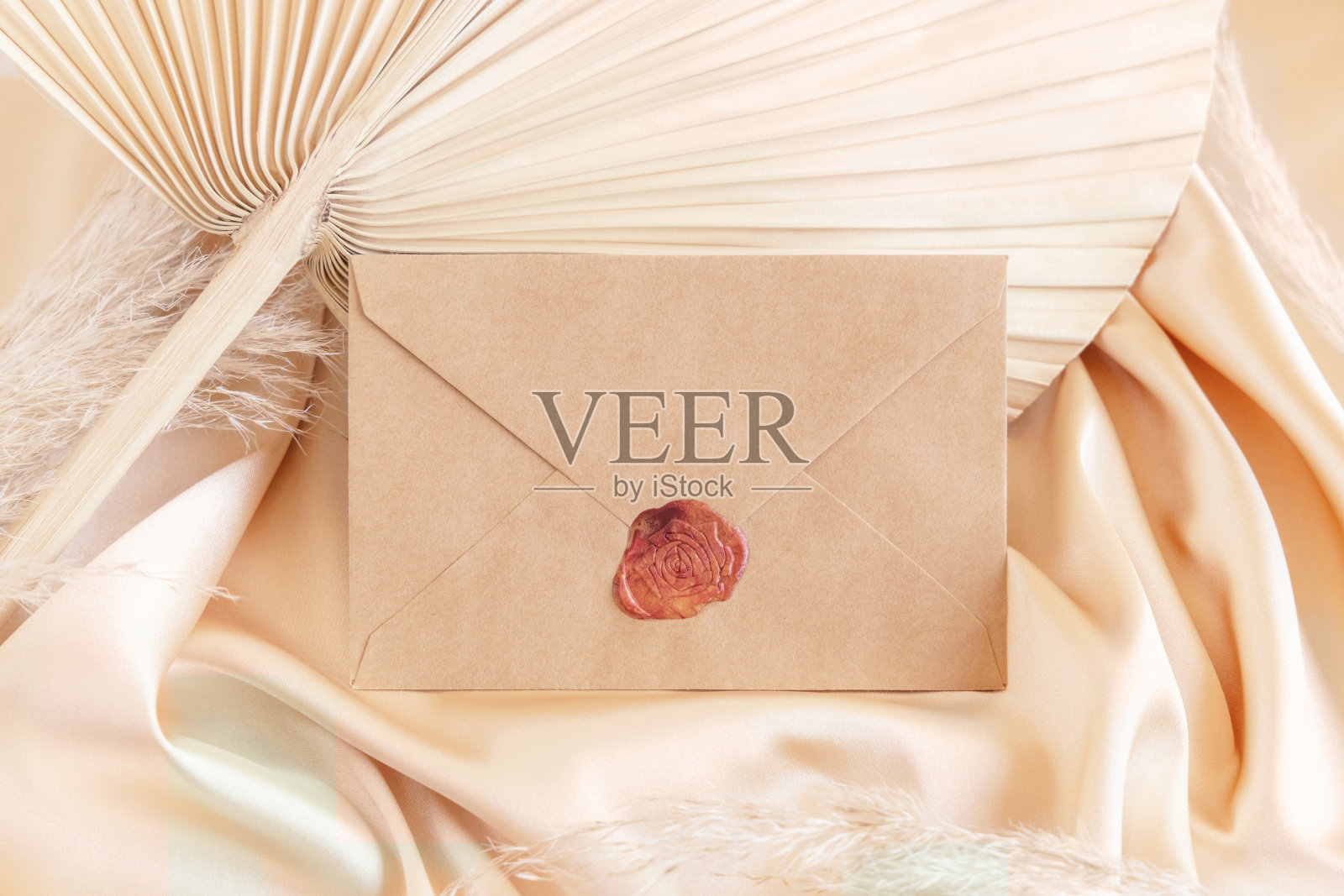 空白信封上的米色缎面织物和干棕榈叶接近,问候或婚礼模型照片摄影图片