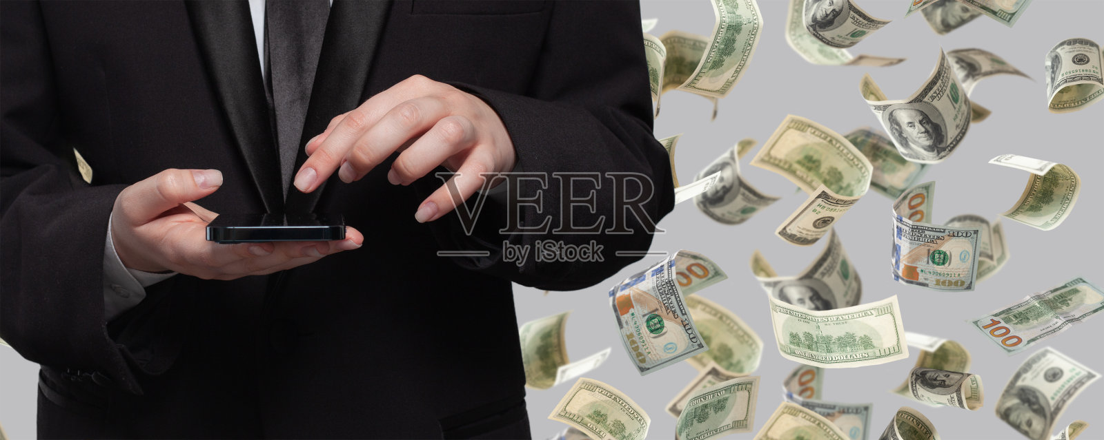 商人在灰色背景下的钱雨下用手机工作照片摄影图片