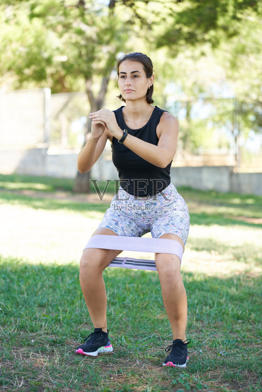 年轻女子在城市公园里用弹力带做伸展运动,做深蹲运动,保持健康。照片摄影图片