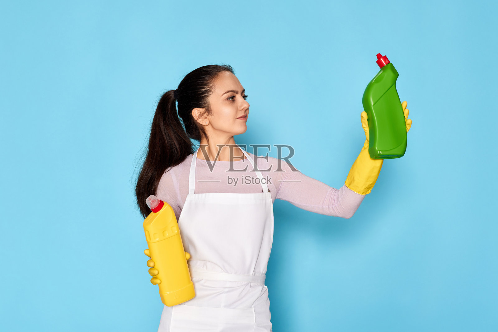 戴着手套和围裙的妇女在两种清洁产品之间选择照片摄影图片