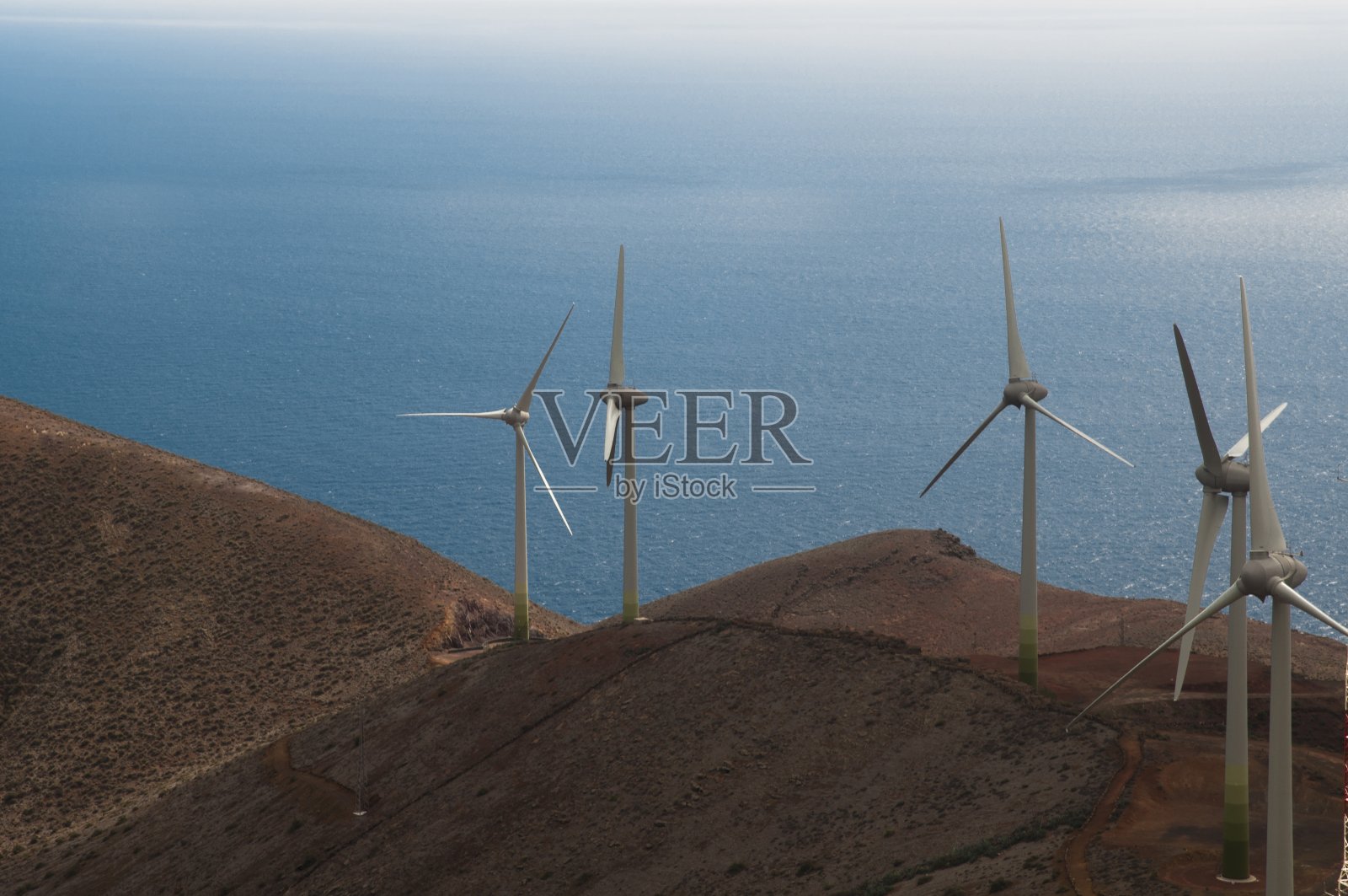 大海被群山环绕,风车覆盖在蓝天和阳光下照片摄影图片