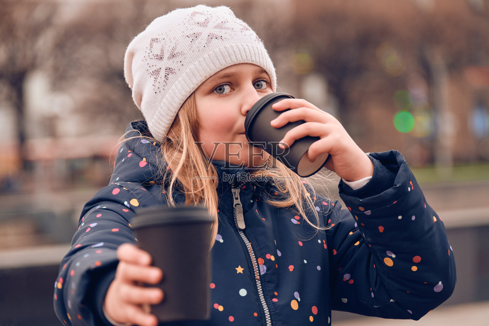 早春,10 - 11岁的女孩在街上喝可可。快乐的孩子拿着一次性杯子,手里拿着饮料照片摄影图片