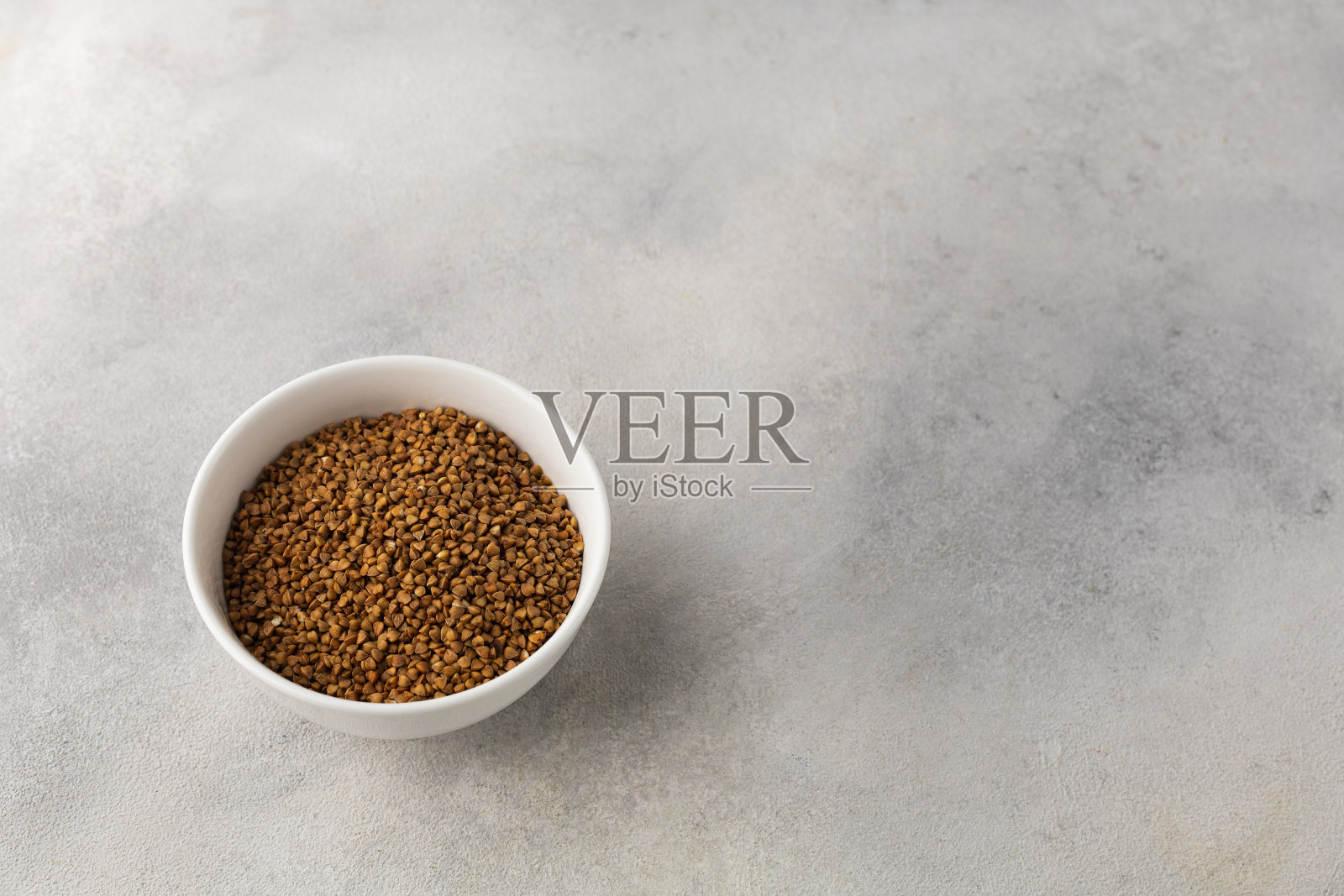 在浅灰色的背景上煮前的一碗干荞麦照片摄影图片