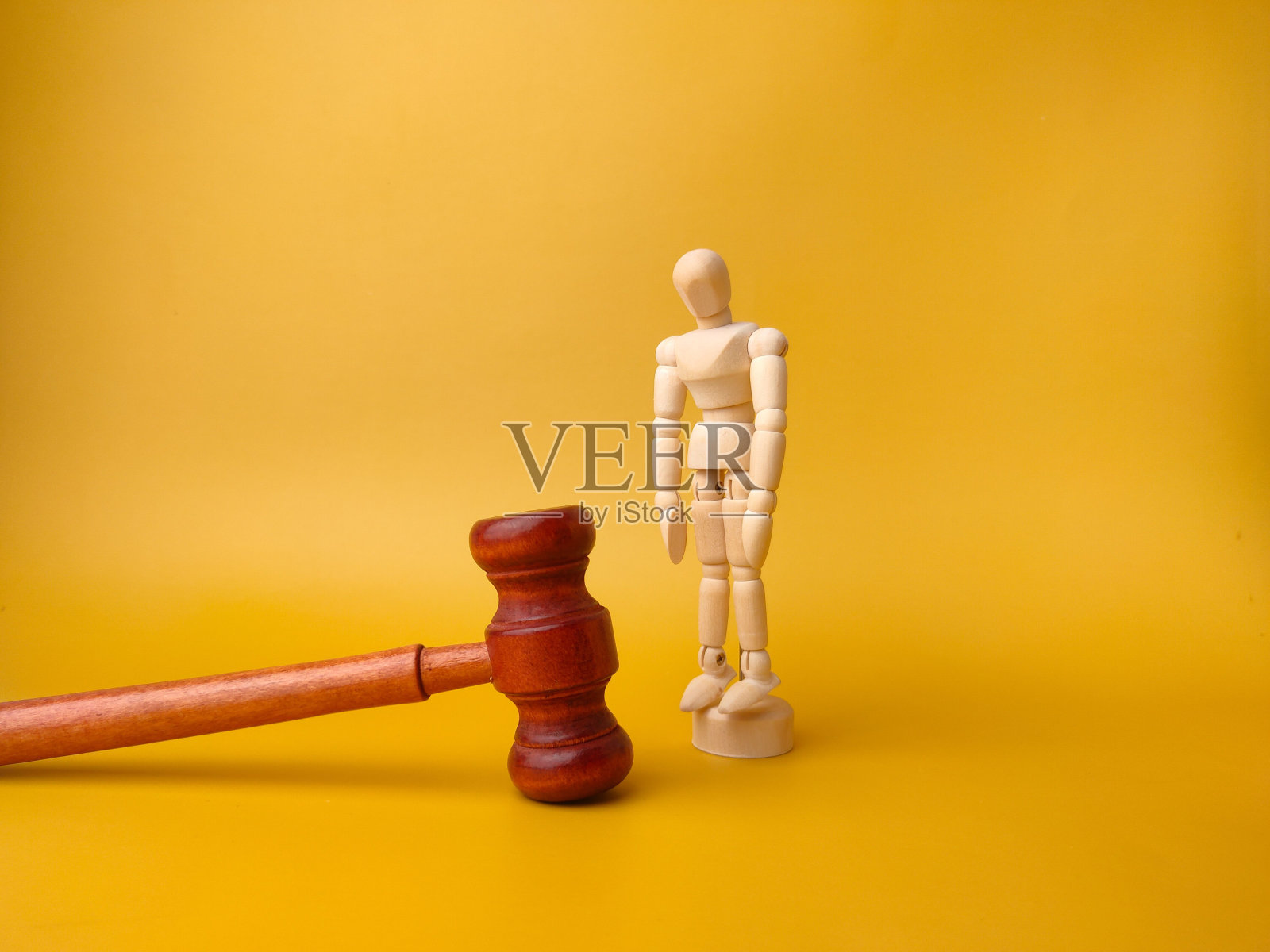 黄色背景上的木制人体模型和木槌 - 法律概念照片摄影图片