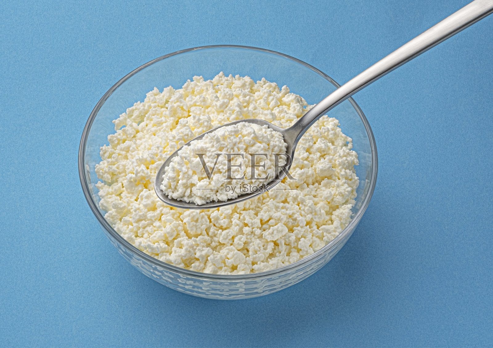 一碗松软干酪,蓝色底色的勺子照片摄影图片