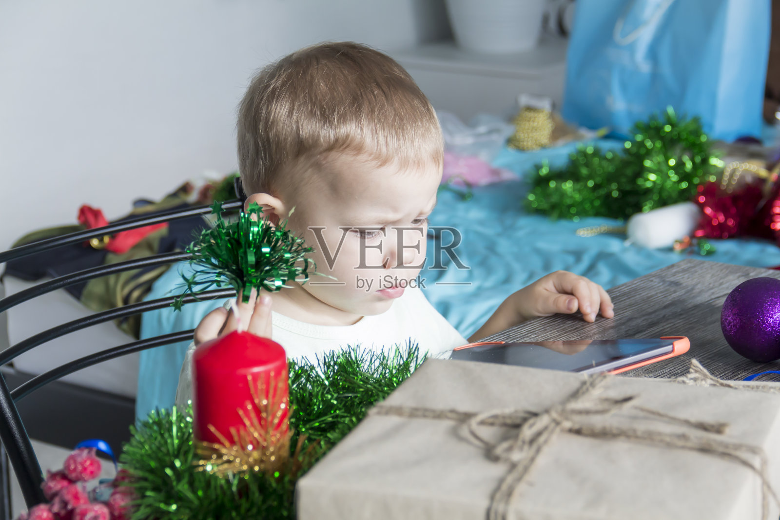 一个带着圣诞礼物的小孩正坐在一张新年木桌前,手里拿着一块写字板。照片摄影图片