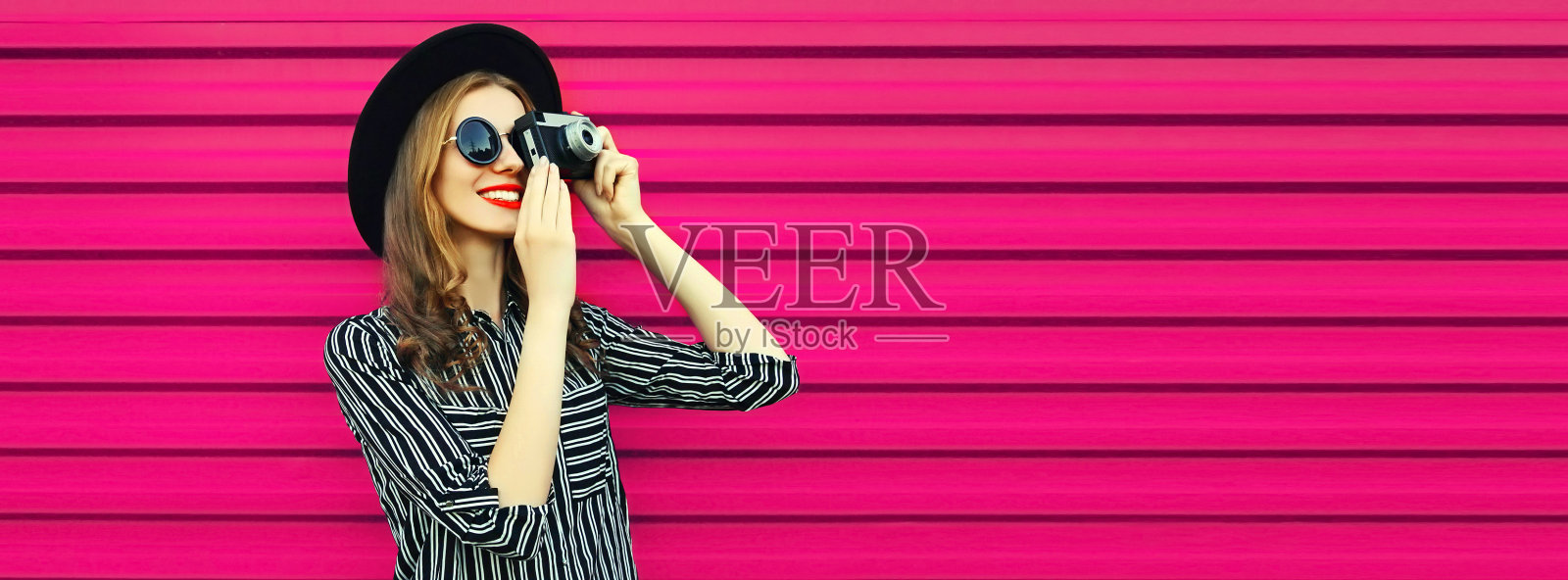 肖像快乐微笑的年轻女摄影师与胶卷相机在粉红色的背景照片摄影图片