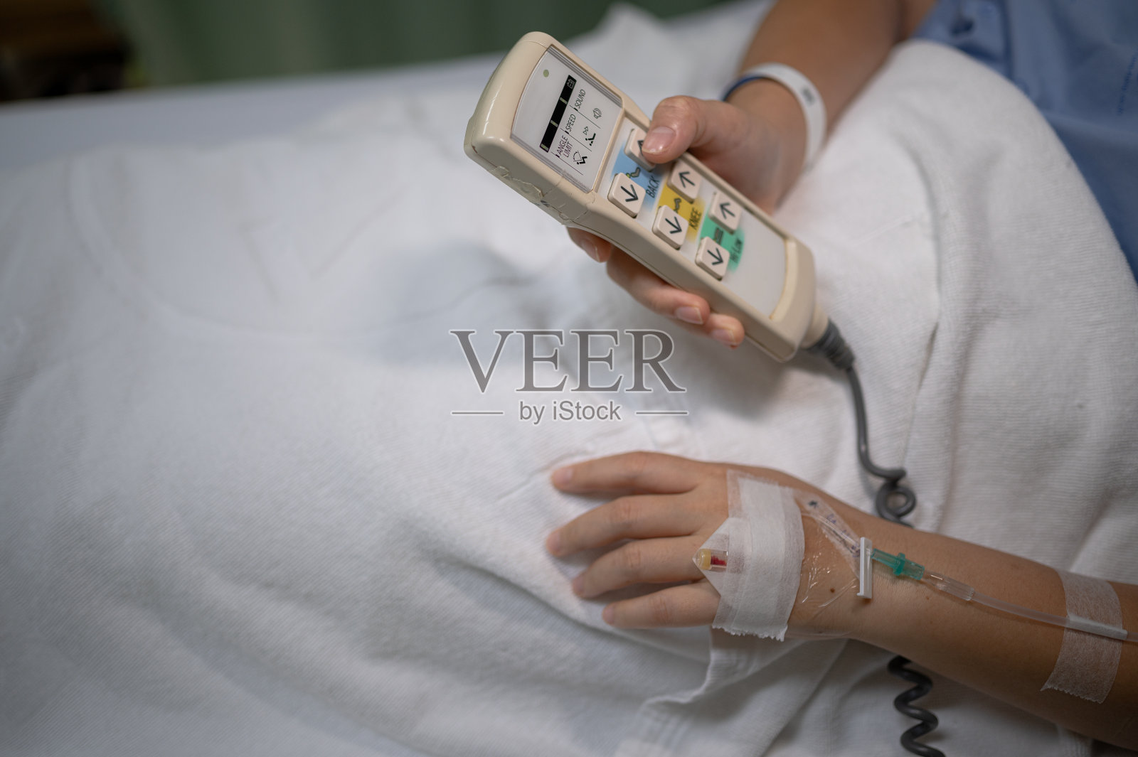 一个女医院病人的手在床上使用遥控器定位她的床的细节。照片摄影图片
