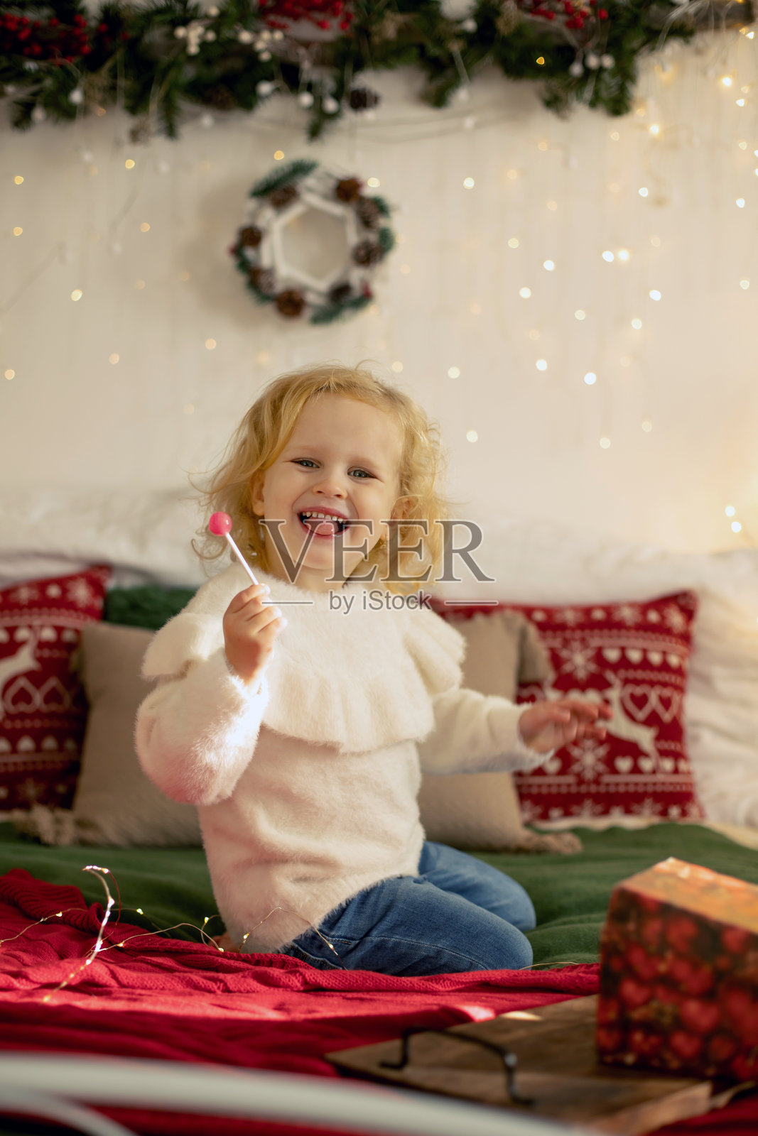 可爱的小卷毛女孩在冬天的圣诞毛衣,坐在舒适的房间,为圣诞节装饰照片摄影图片