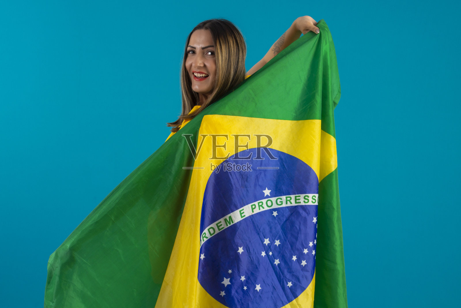 巴西女支持者,穿着印有巴西国旗的衬衫。巴西球迷在工作室的照片与蓝色背景和巴西的颜色。照片摄影图片