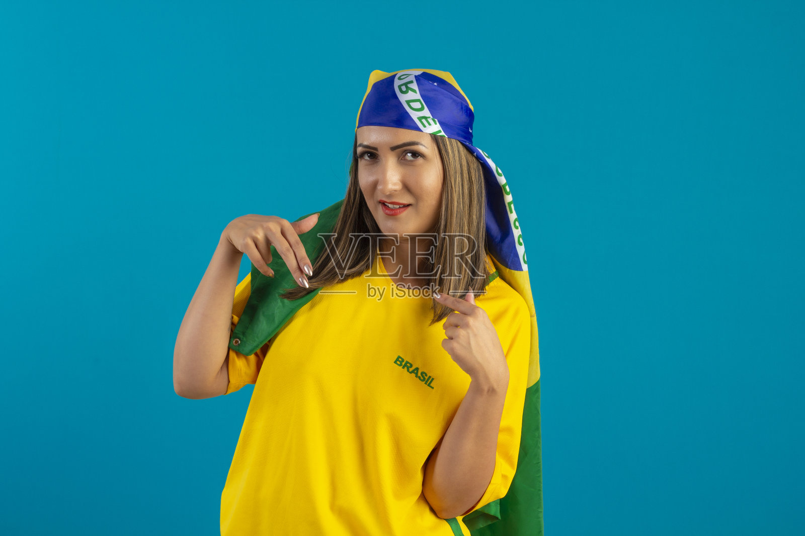巴西女支持者,穿着印有巴西国旗的衬衫。巴西球迷在工作室的照片与蓝色背景和巴西的颜色。照片摄影图片