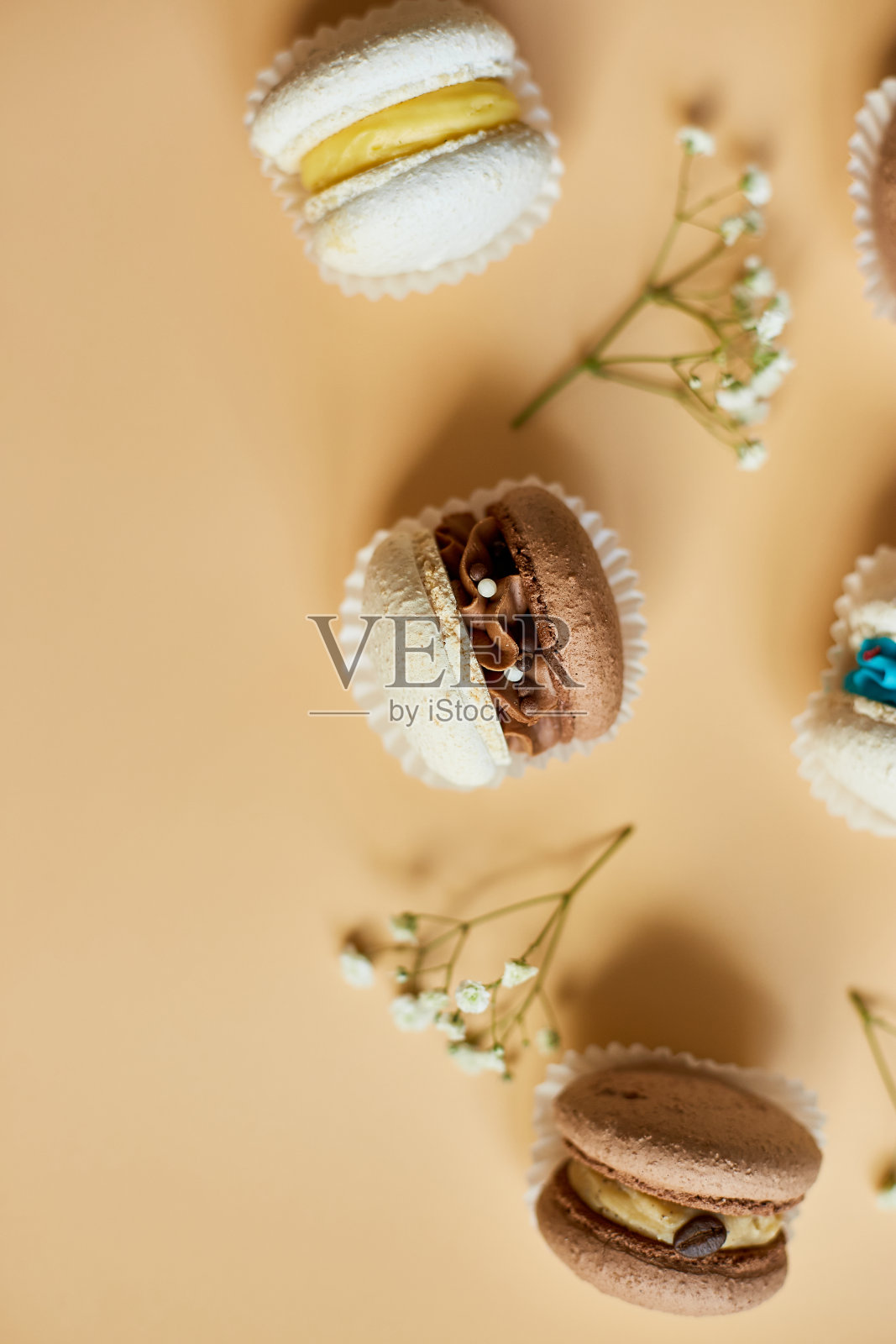 顶视图设置不同的法国饼干马卡龙,蛋糕马卡龙与花朵在橙色背景,彩色杏仁饼干,柔和的颜色照片摄影图片