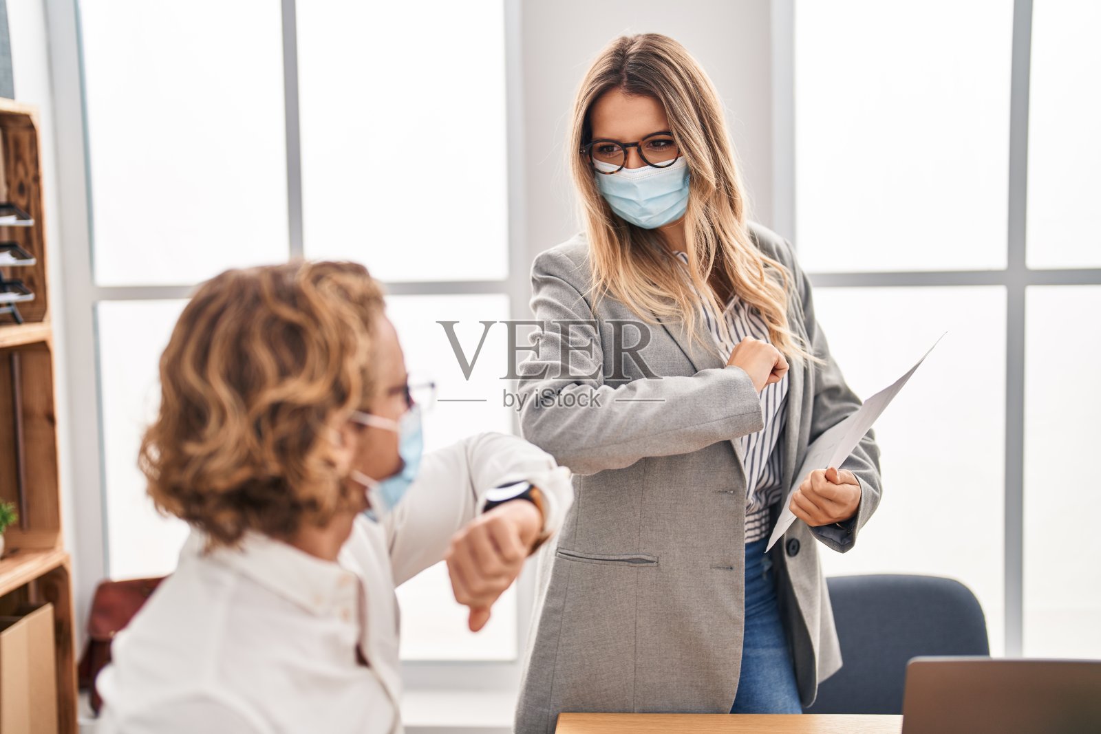 戴着医用口罩的男女工作人员在办公室进行安全问候照片摄影图片