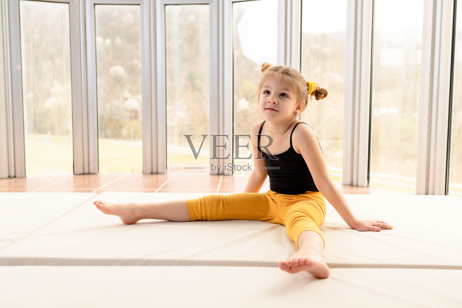 可爱的小女孩穿着运动服坐在健身房,看起来很无聊照片摄影图片