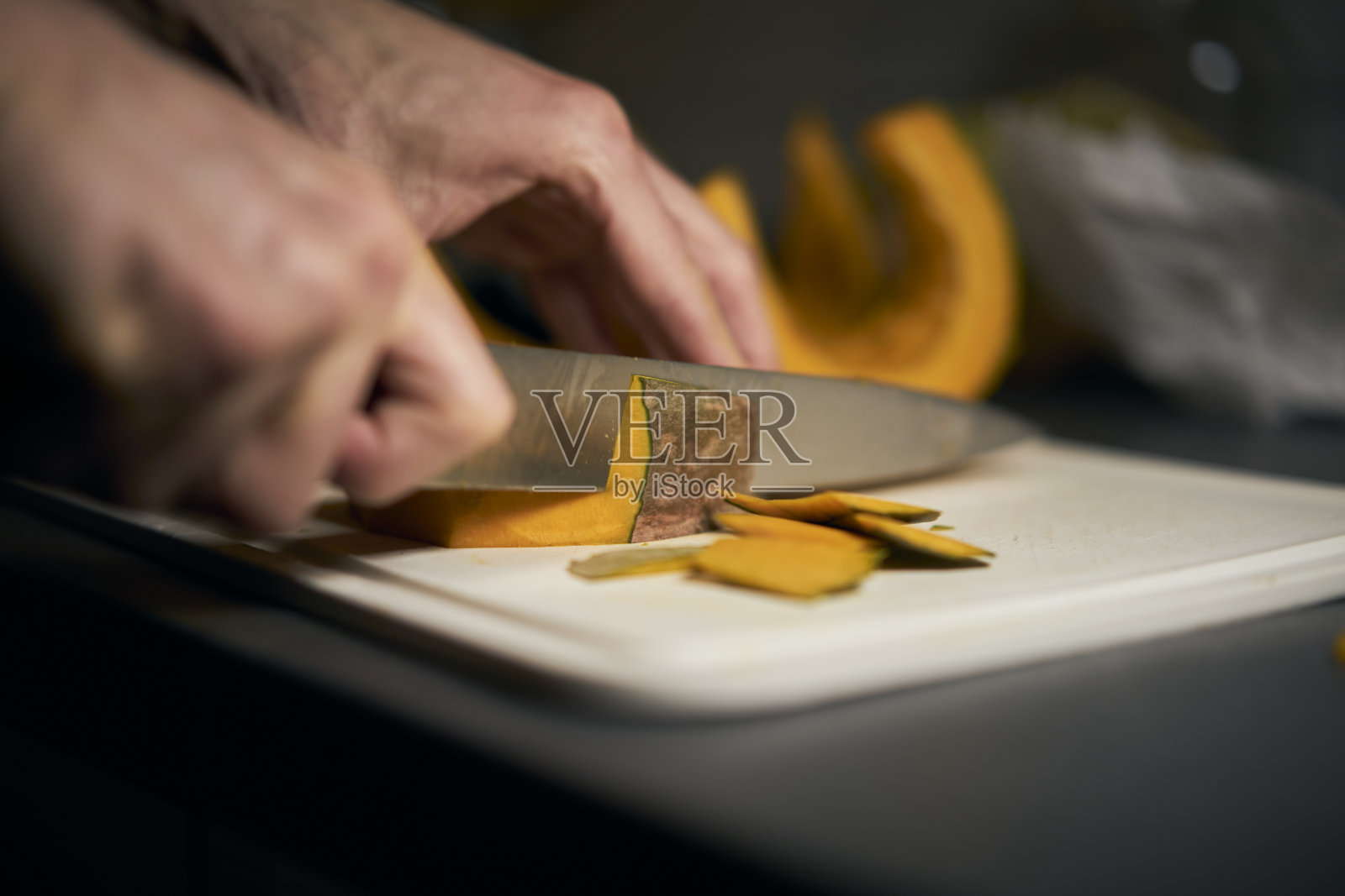 男人把一个凉爽的圆形南瓜切成小块,背景是黑色的。照片摄影图片