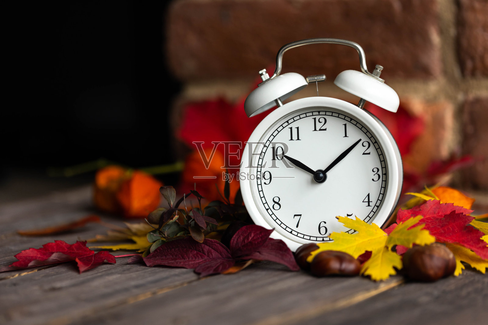 秋冬时间观念改变。秋天用复古的闹钟组成,鲜黄红叶,胡桃木。背景是砖墙。舒适的家庭氛围。特写镜头照片摄影图片