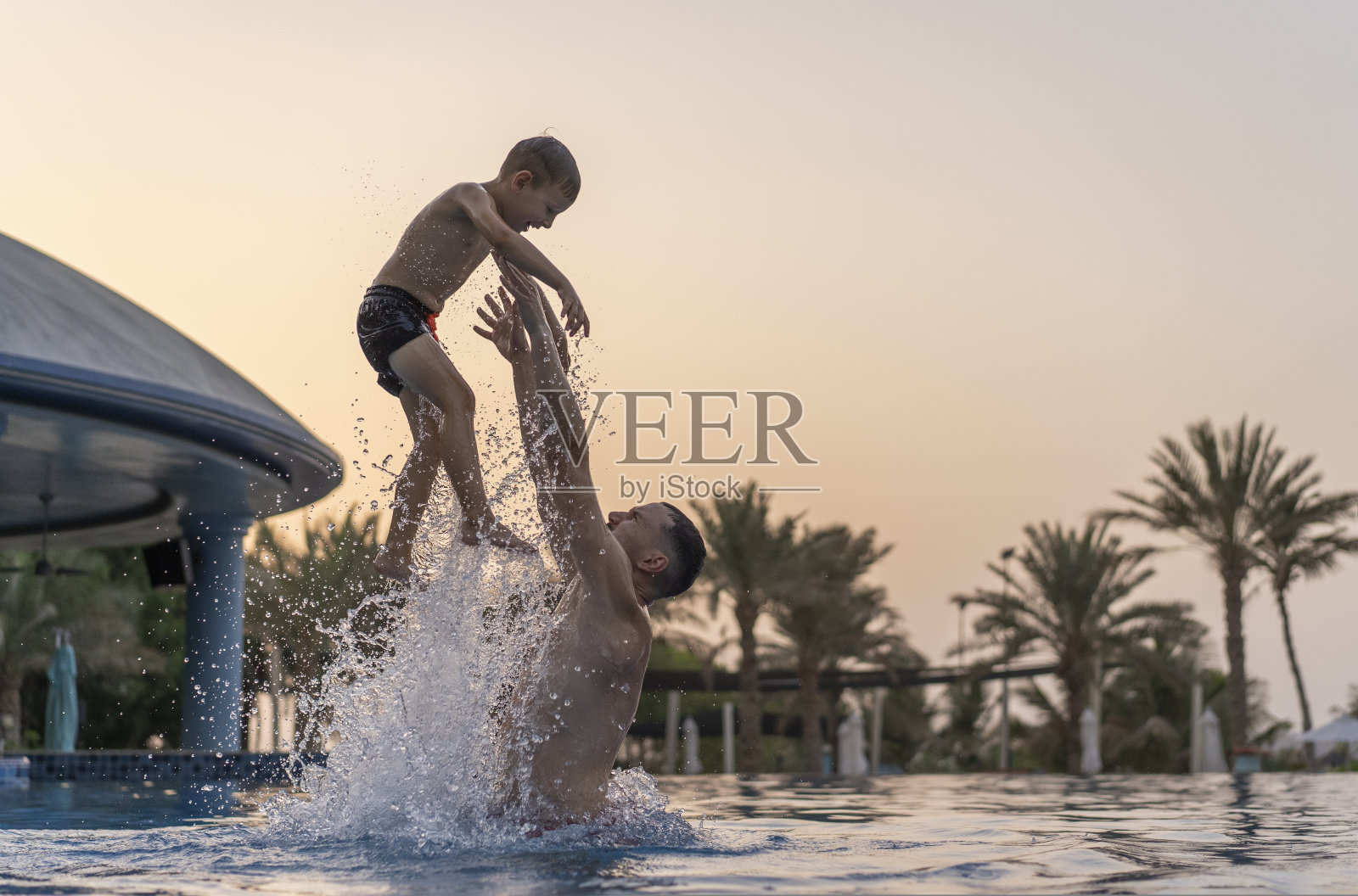 爸爸和儿子在游泳池里玩耍,父亲把儿子抛起来照片摄影图片