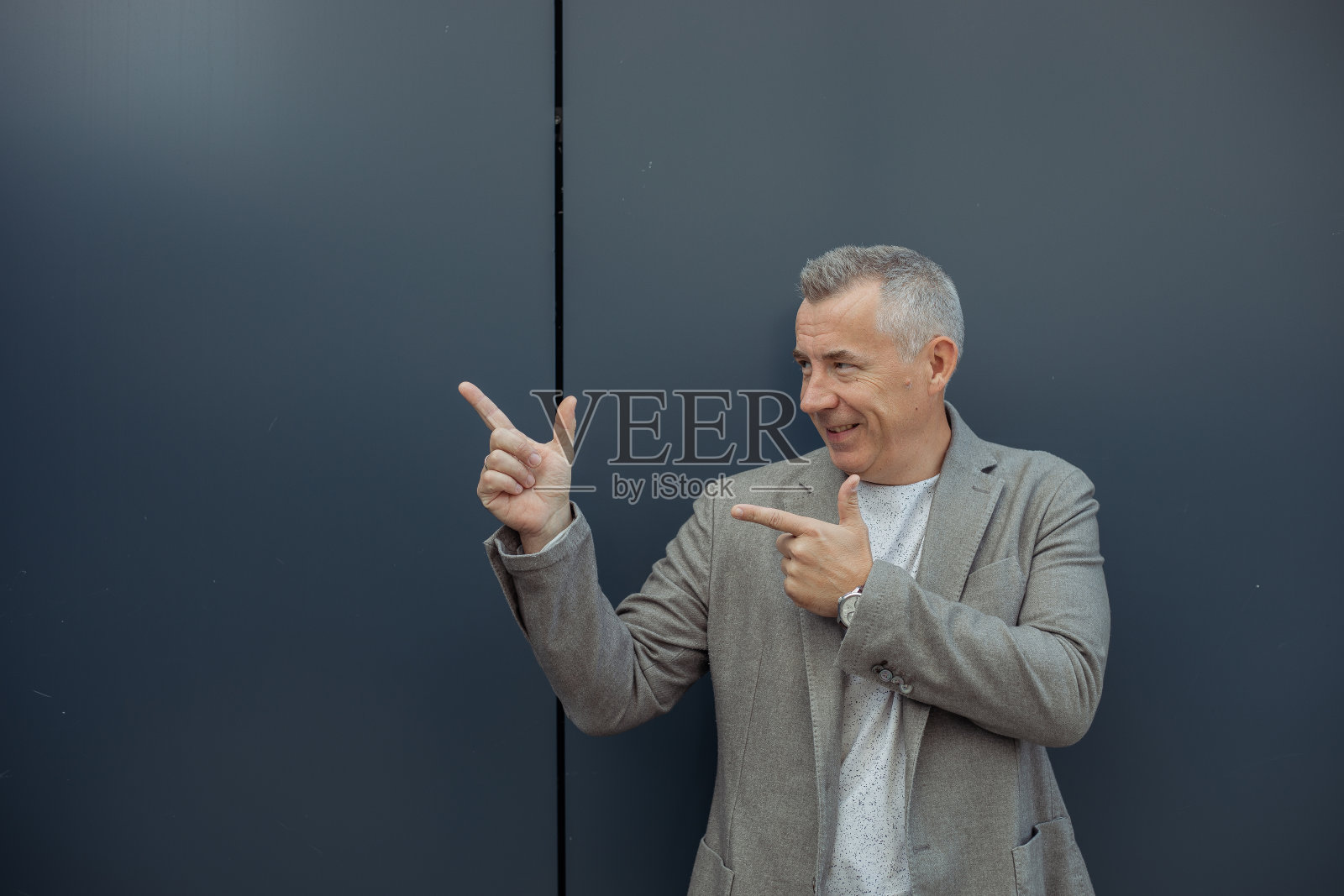 腹部微笑,自信,头发花白的男人看向别处,用食指显示,呈现出空空的空间作为产品照片摄影图片