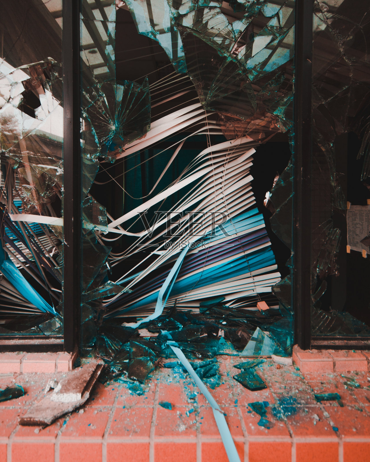一扇破碎的窗户,白色百叶窗被毁坏,玻璃碎片散落在地上照片摄影图片