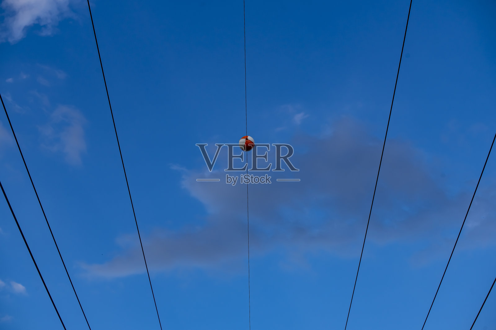 低角拍摄的红白相间的球悬挂在高压电线上,鹳鸟飞过照片摄影图片