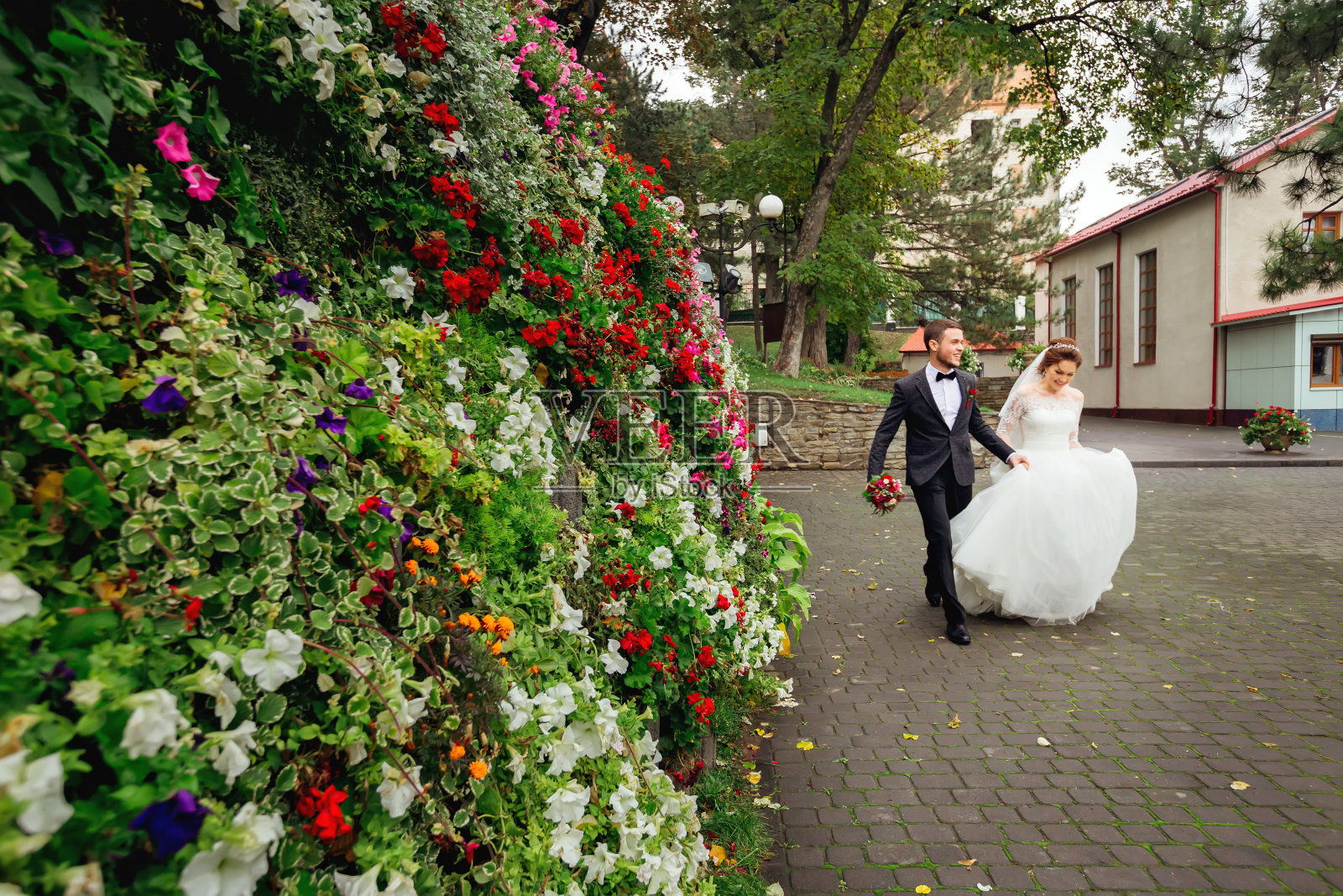 在花木建筑的背景下,幸福的新婚夫妇在公园里跑来跑去照片摄影图片