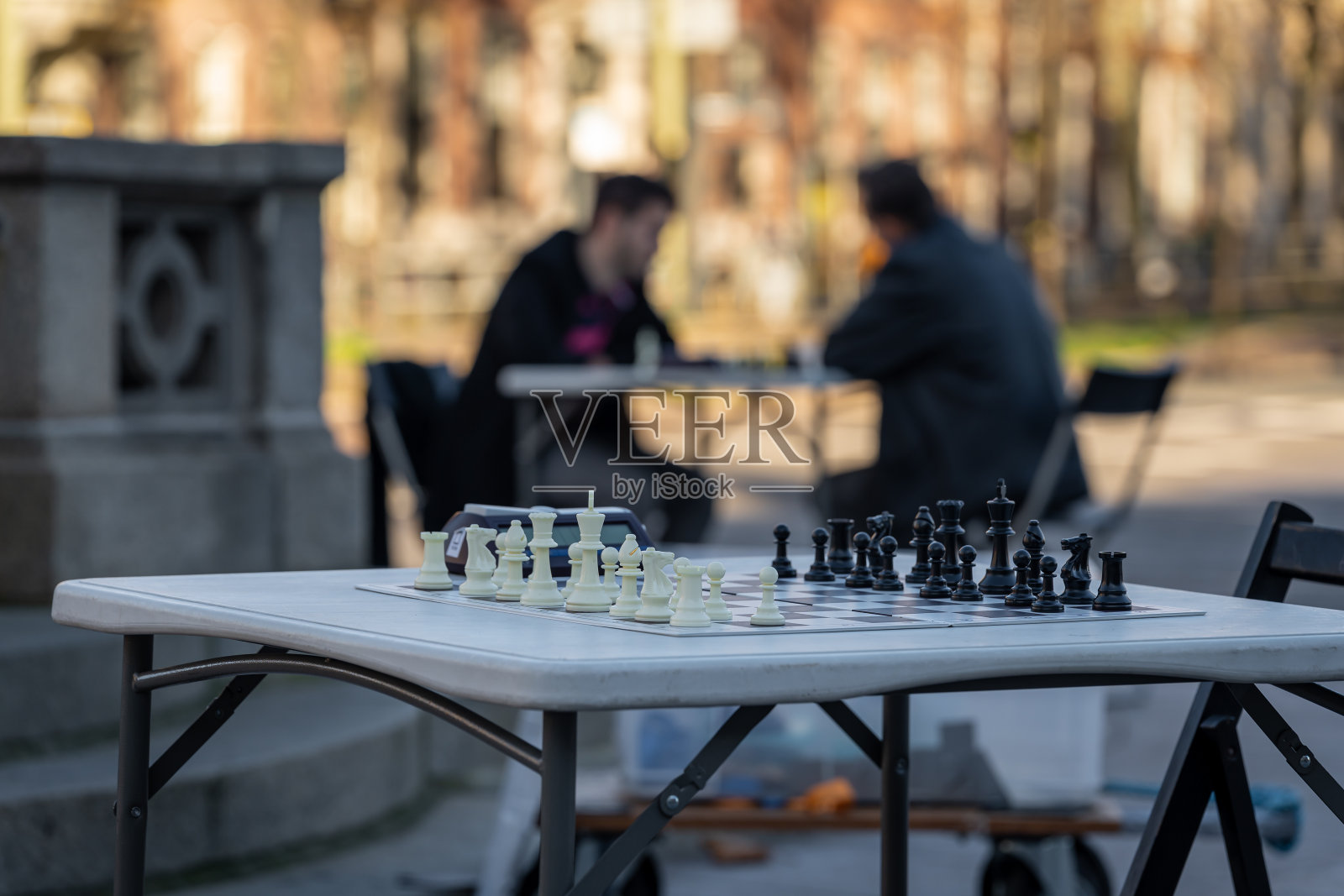 在街上的棋盘上准备下棋。背景模糊,棋手的剪影在桌子上。照片摄影图片