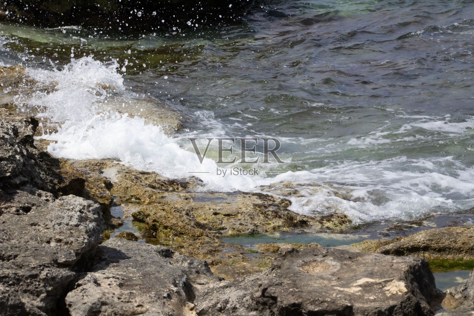 在一个阳光明媚的日子里,海浪拍打在沙滩上的石头上的特写照片摄影图片