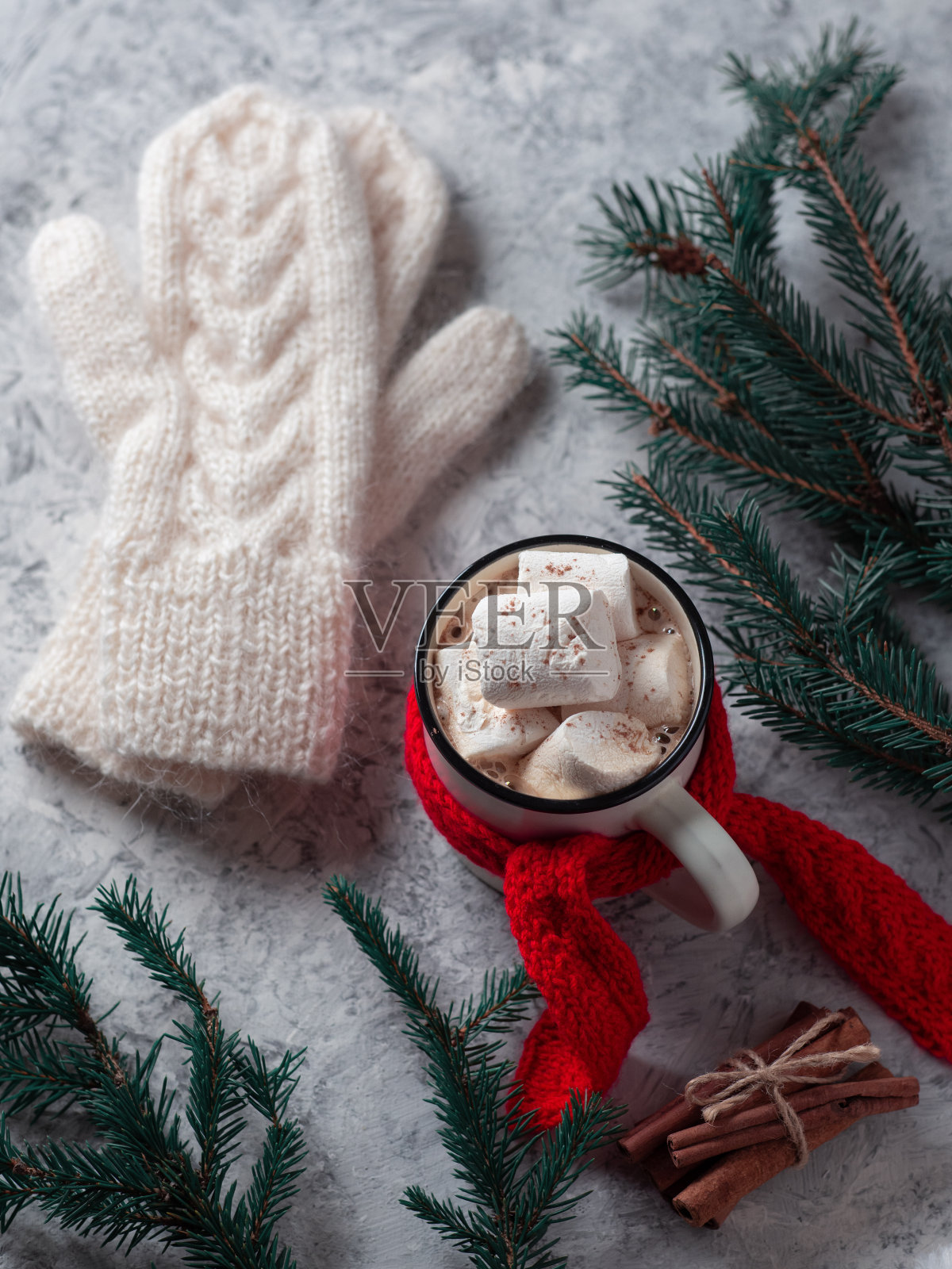 热巧克力或咖啡配棉花糖放在白色的混凝土桌子上,桌上放着圣诞树树枝,戴着温暖的针织手套和红色围巾照片摄影图片