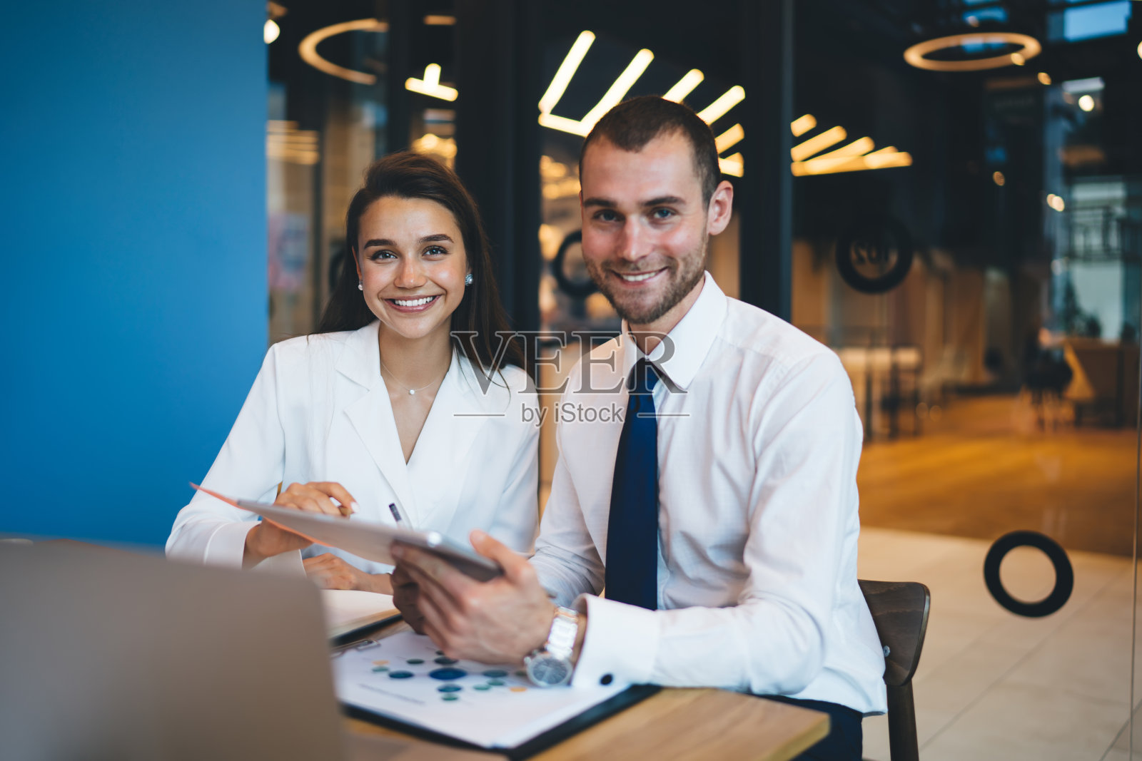 欢快的企业员工坐在有现代科技的桌子前,对着镜头微笑,自信的专业分析师享受业务项目合作简报会照片摄影图片