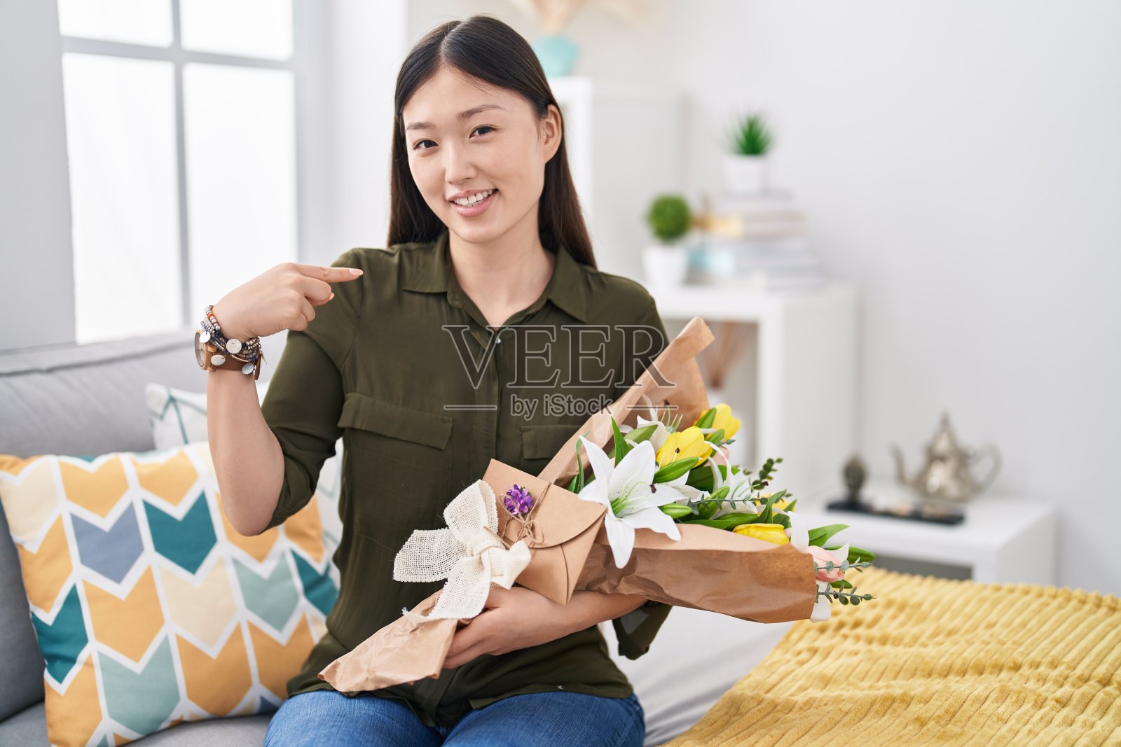 中国年轻女子手持一束白花,面带微笑,自信地用手指指着自己,骄傲和幸福。照片摄影图片