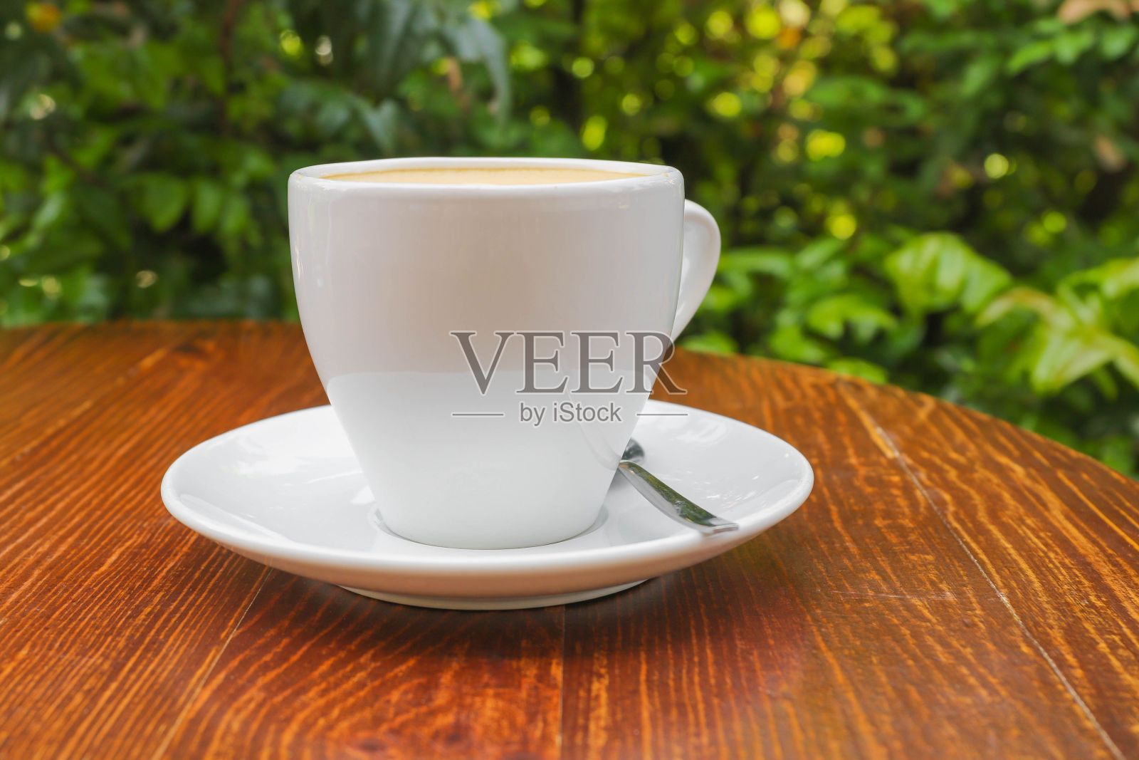 在绿树成荫的背景下,木桌上放着一杯热咖啡照片摄影图片