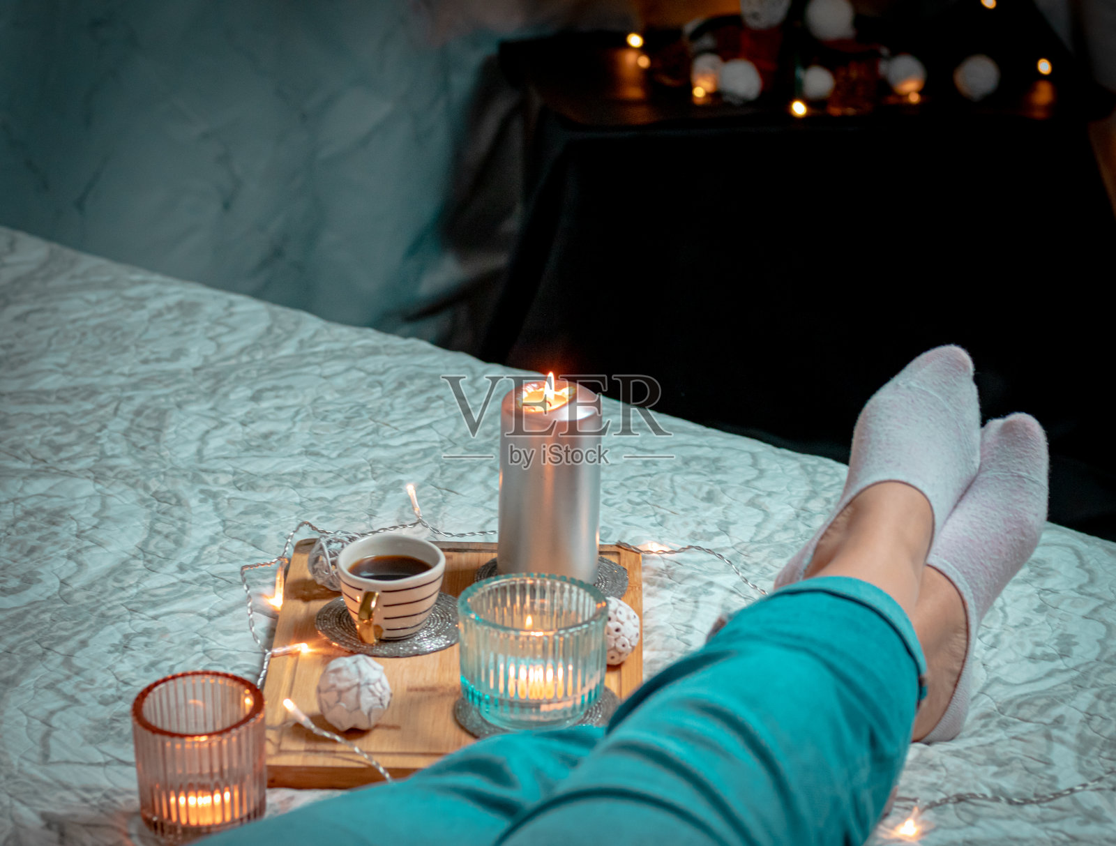 女人穿袜子的腿,一杯卡布奇诺,毯子上的蜡烛和一棵挂满彩灯的圣诞树。家的舒适和舒适的气氛照片摄影图片