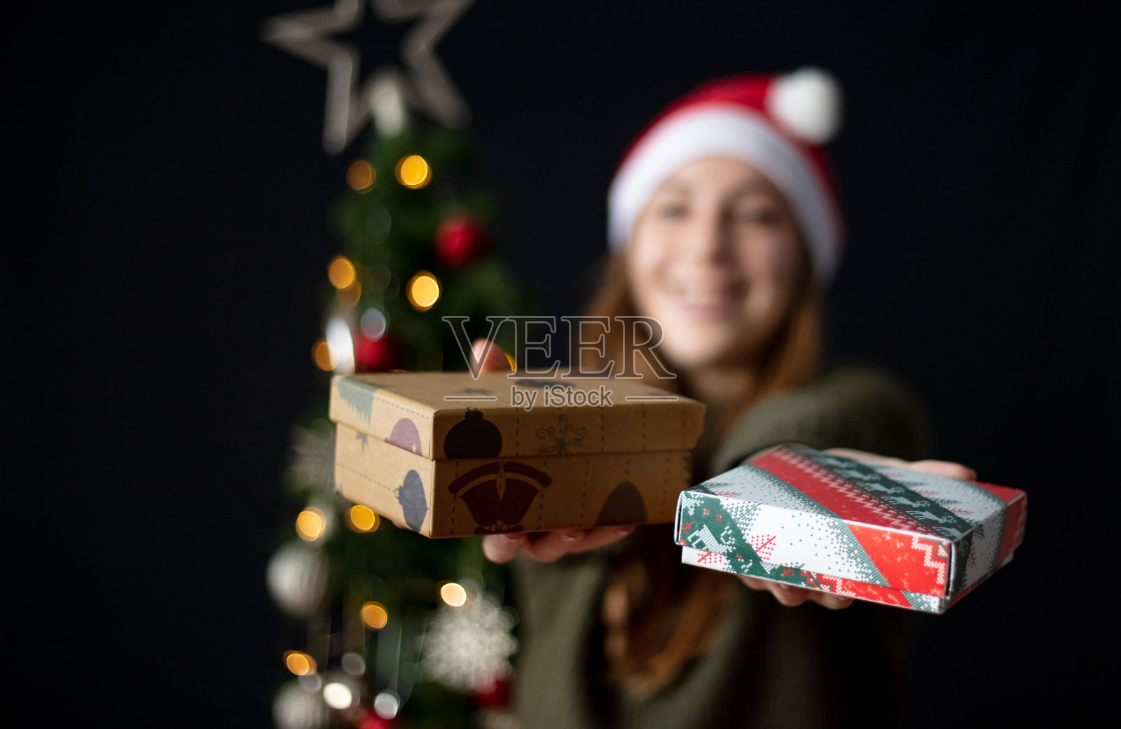 金发女人拿着许多礼物盒在圣诞树前。照片摄影图片
