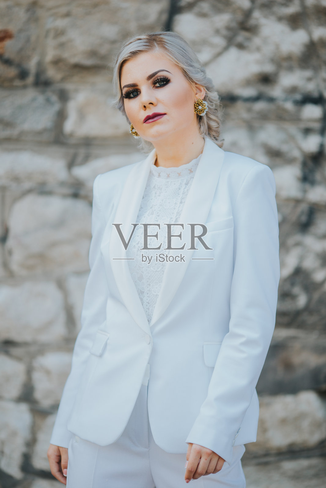 垂直拍摄的金发女性摆姿势穿着优雅的白色长裤套装照片摄影图片