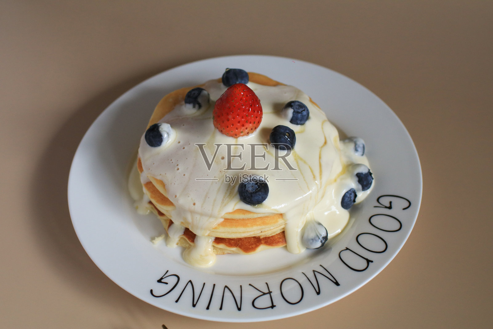 薄饼配蓝莓、草莓和奶油,放在白色盘子里。健康的早晨自制早餐。照片摄影图片