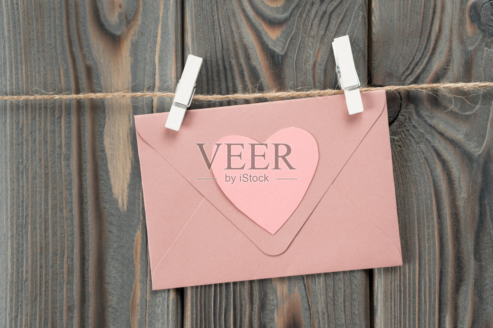 粉色可爱的纸信封,心形挂在绳子上,衣夹在木头背景上。情书照片摄影图片