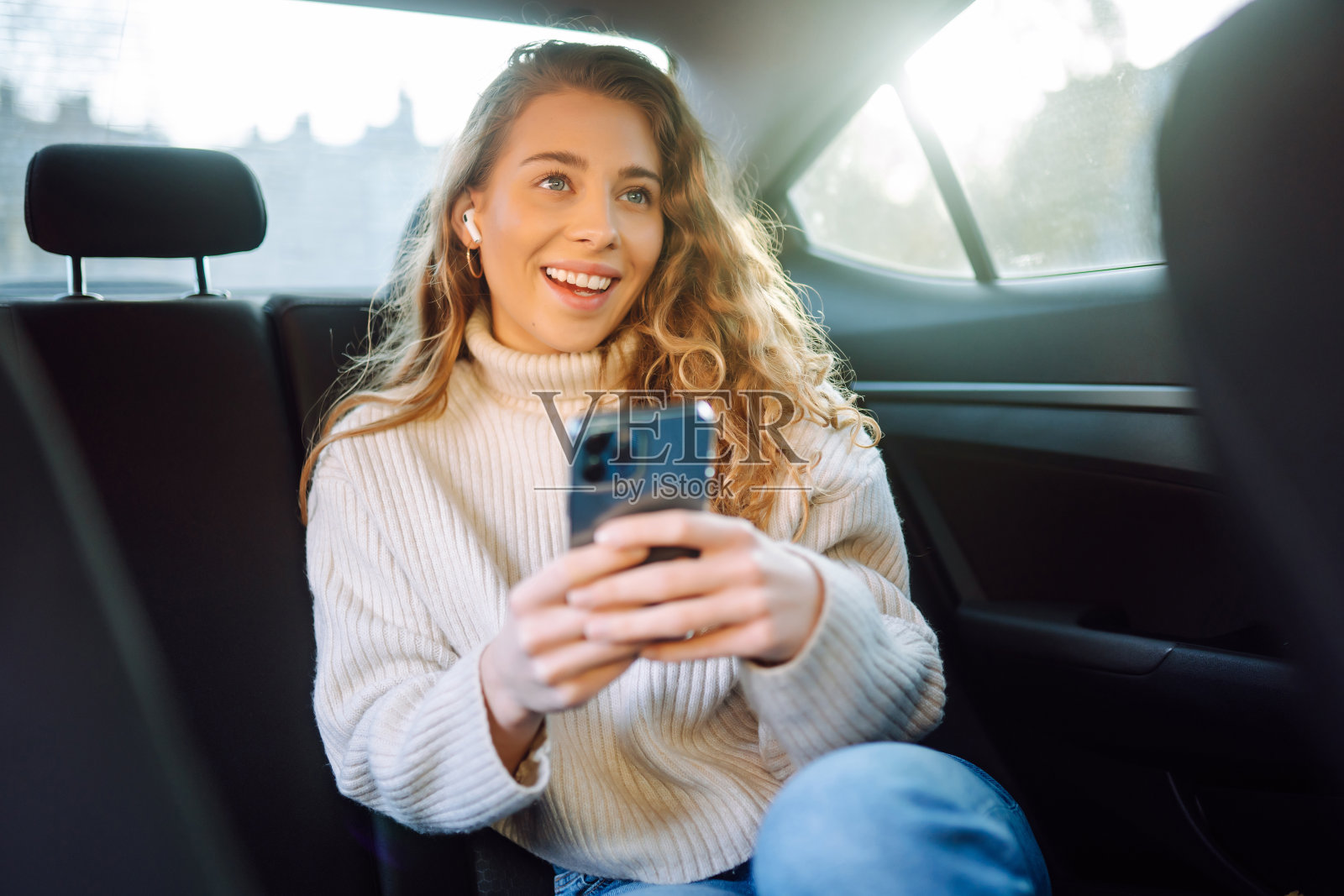 一位美丽的女士坐在汽车后座上微笑着使用智能手机。照片摄影图片