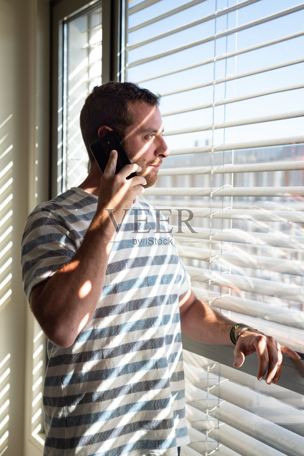 年轻人一边打电话一边看着窗外。照片摄影图片