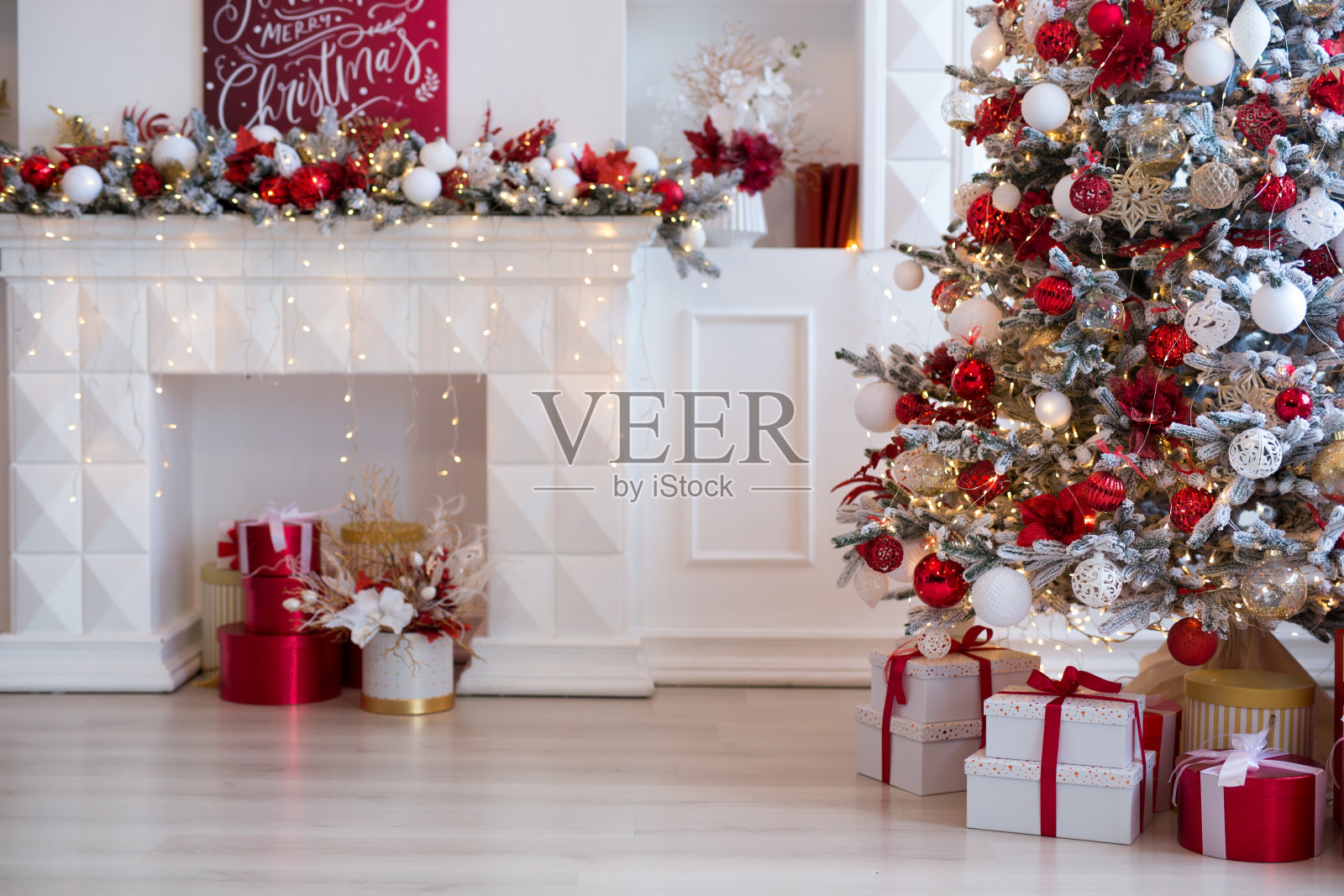 明亮的现代客厅内壁炉,枝形吊灯和舒适的沙发装饰圣诞树和红色礼物照片摄影图片